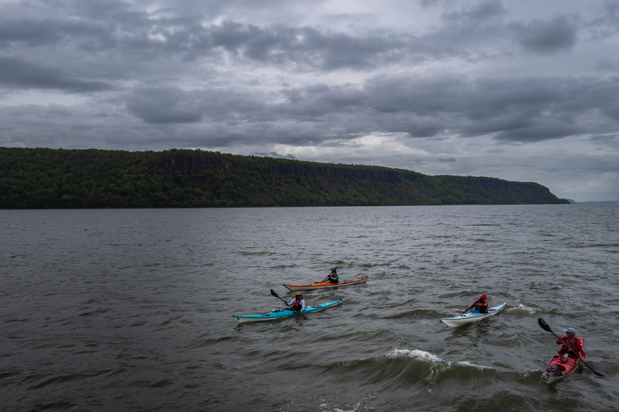 Four boats in loose formation, the lead paddler in red pulling ahead into the wind.