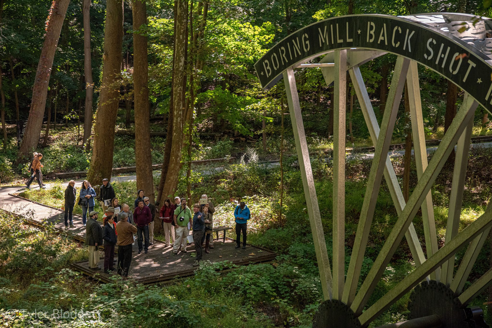 Visitors gather on the boardwalk beneath a steel outline of the boring mill's back shot wheel.