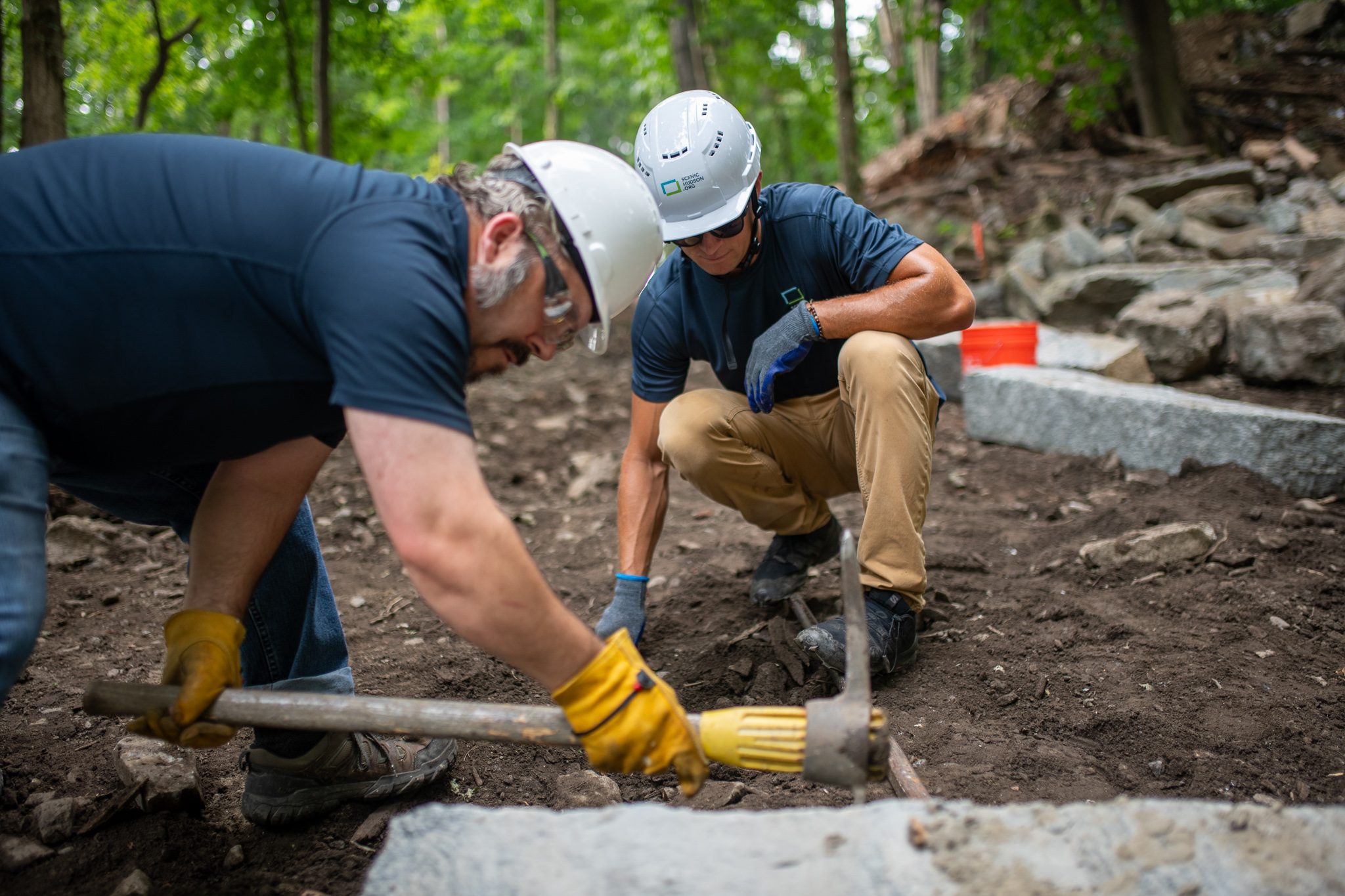One man taps with a hammer while his partner guides the stone.
