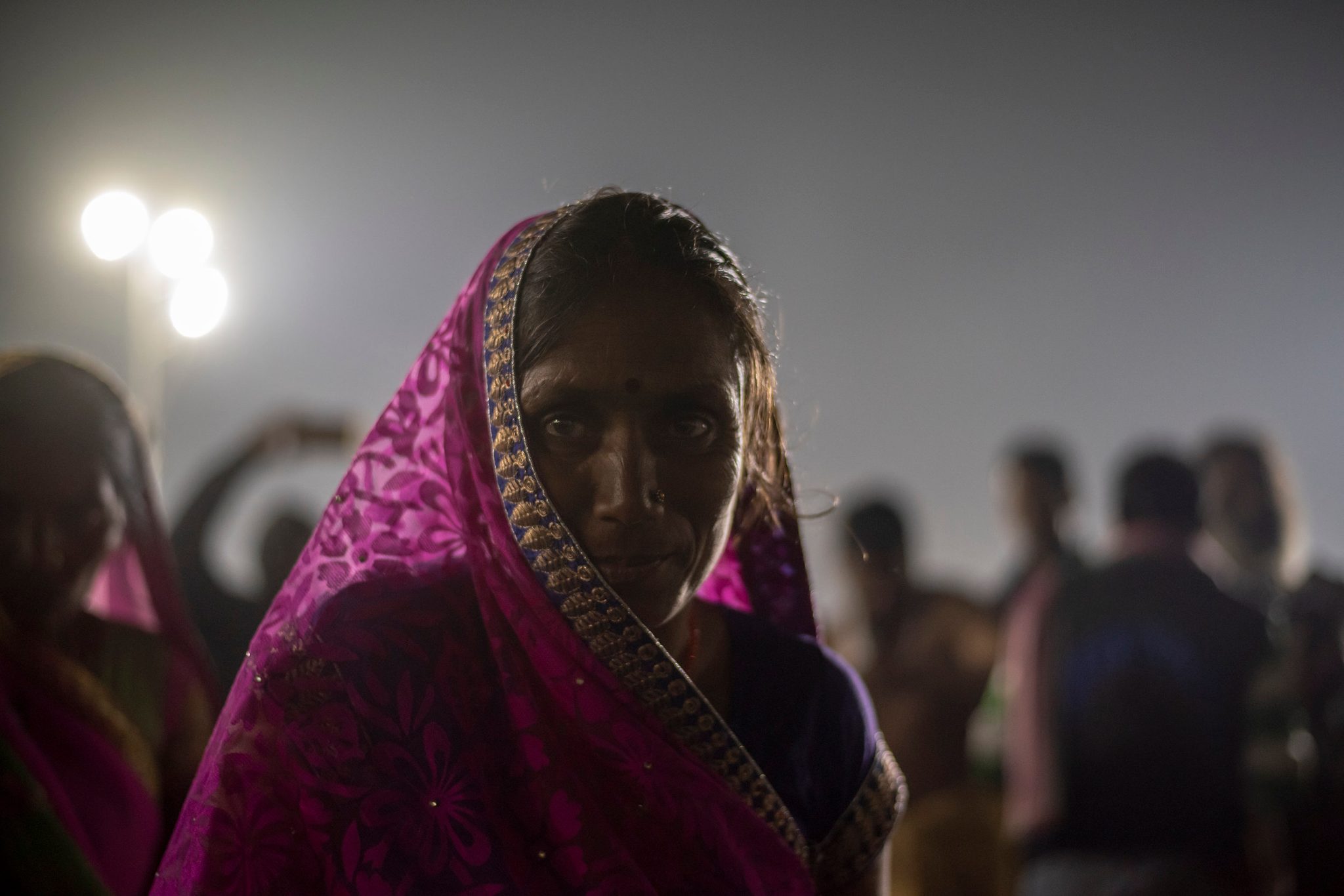 A woman in magenta pauses beneath the floodlights as the night crowd moves past her.