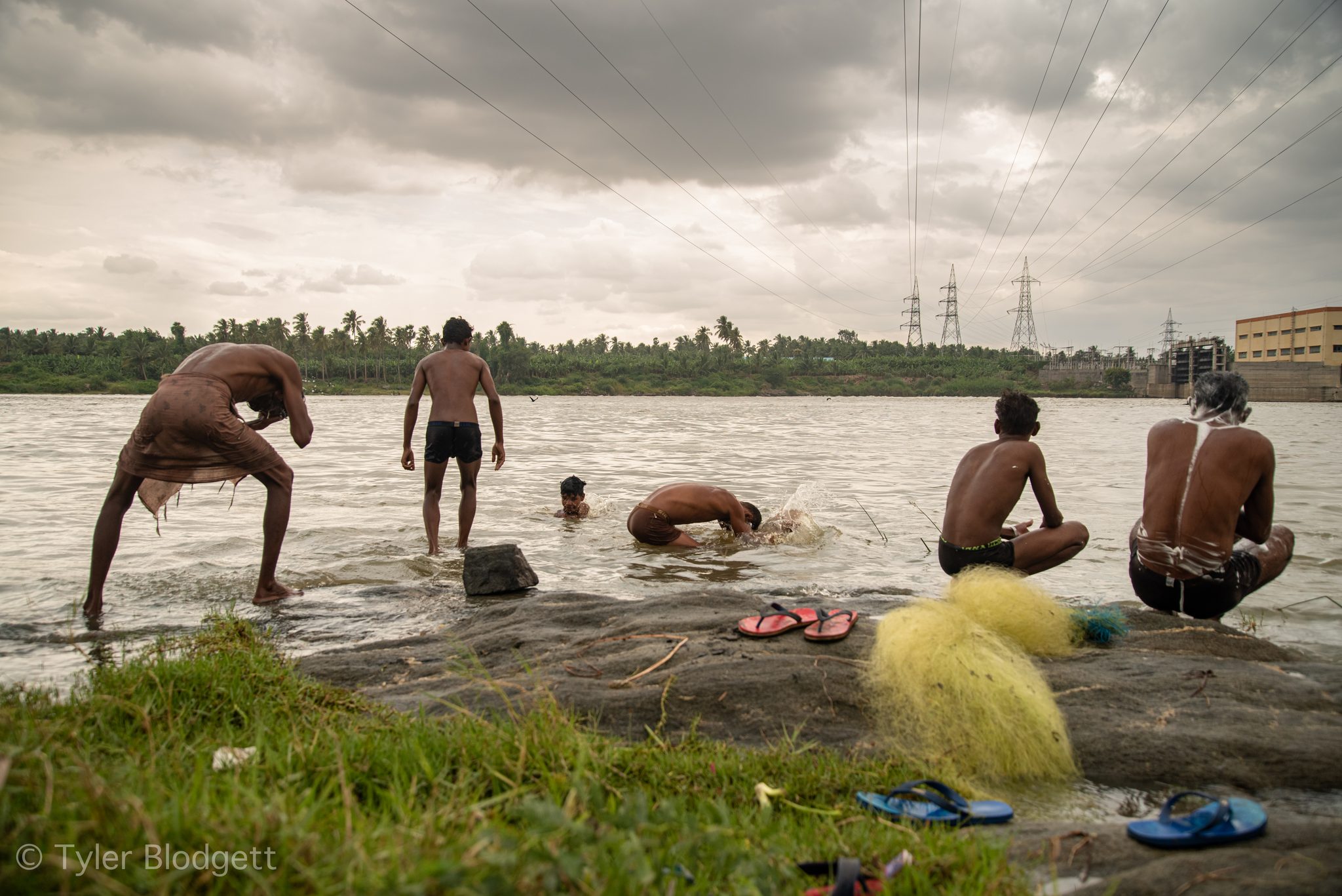 One man dips into the river while the others wash on the rocks.