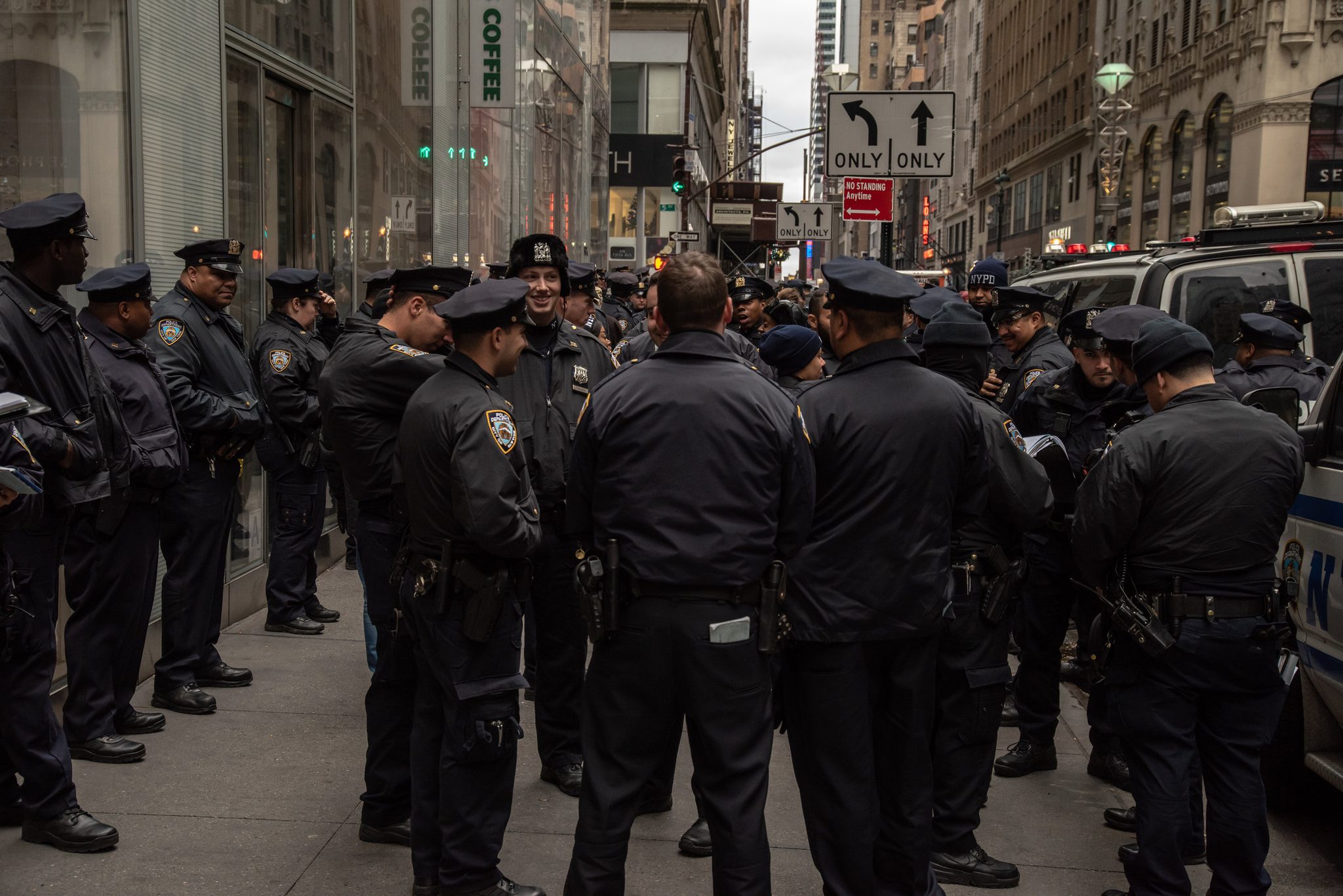 Officers gather by the dozen on the corner, caps and jackets as far down the block as the eye can see.