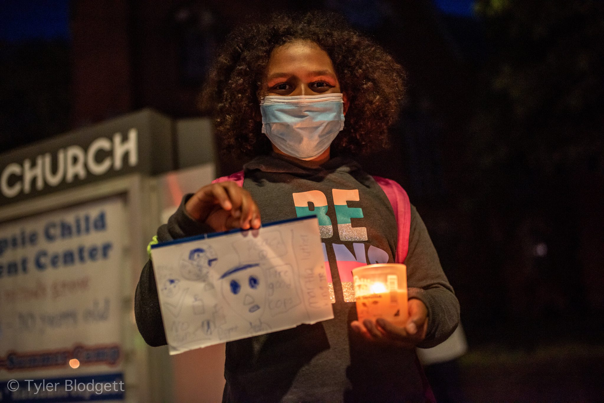 A girl holds up her drawing and a candle outside the church.