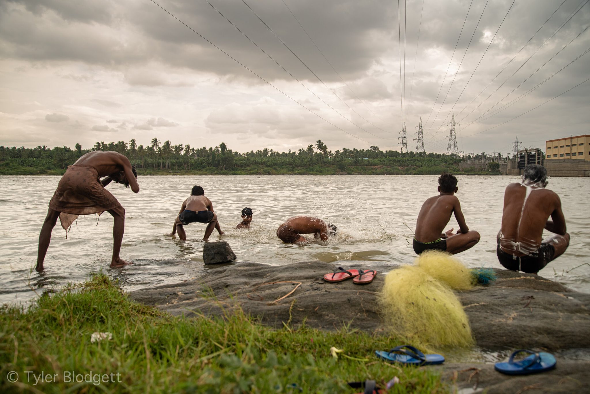 Men bathe and wash in the river while their nets dry in a yellow heap on the rocks.