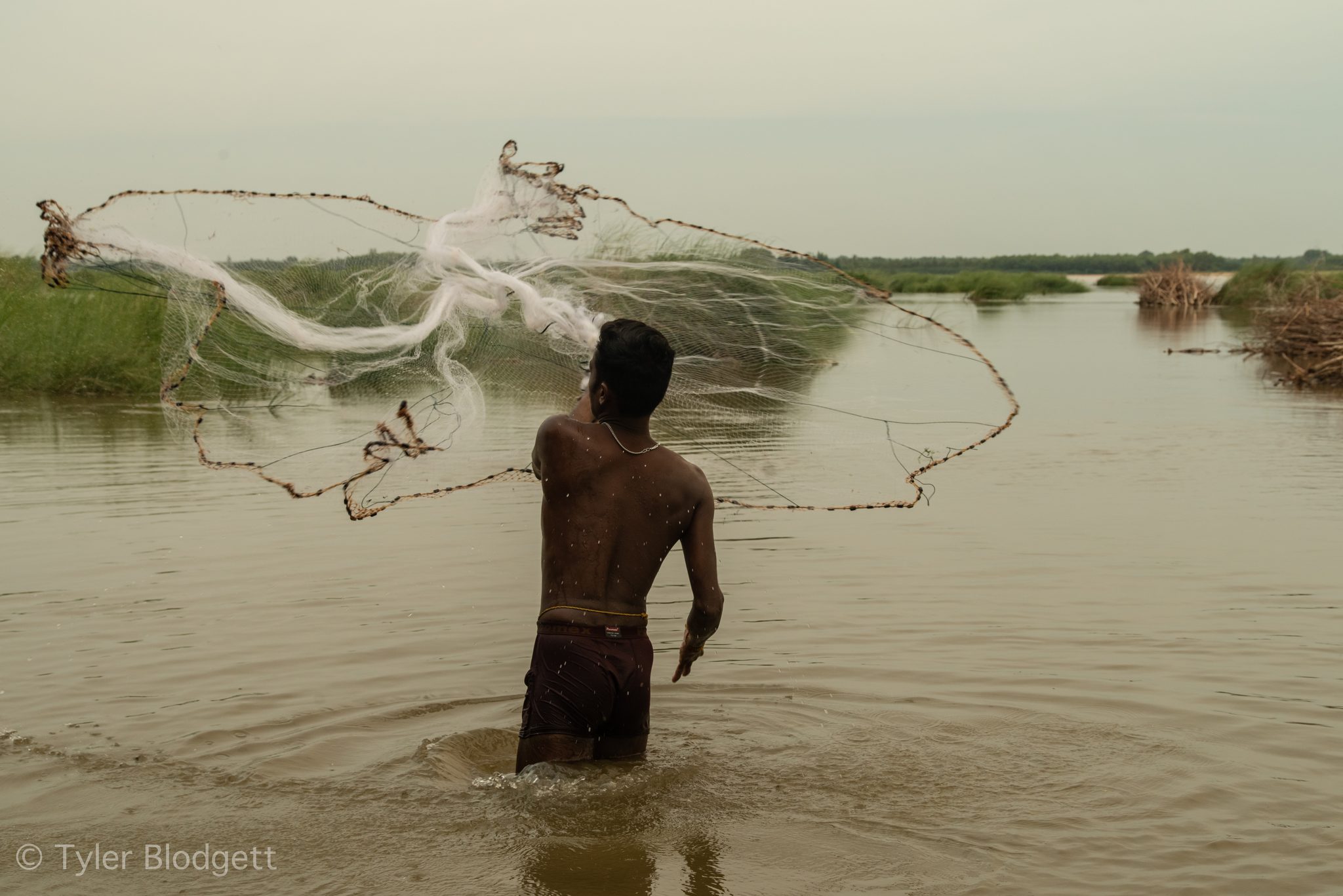The net flies open over the water as he casts.