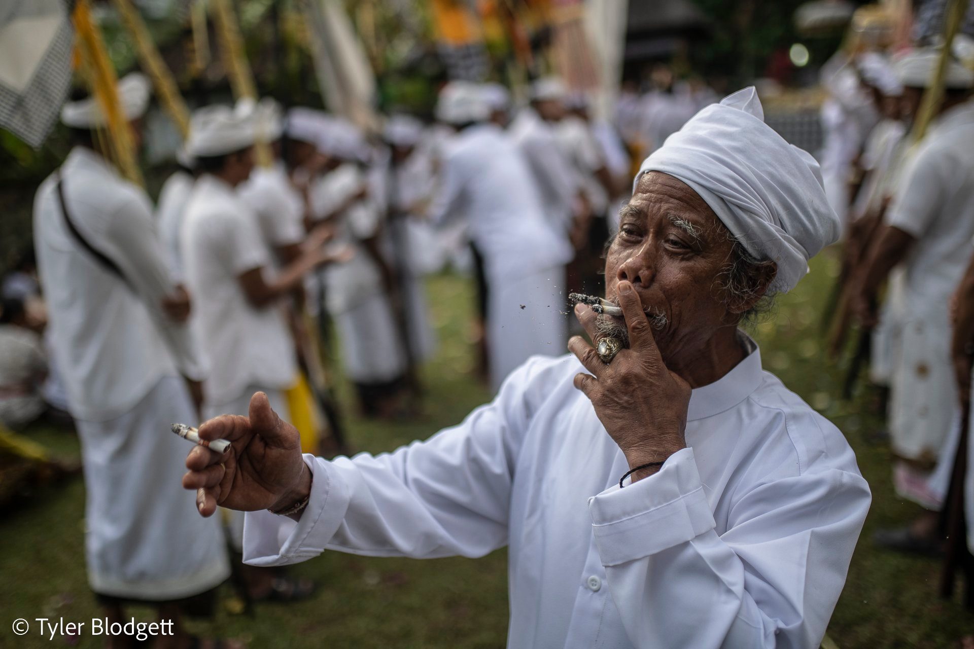 An elder in white, cigarette in hand, lets the ceremony swirl around him.