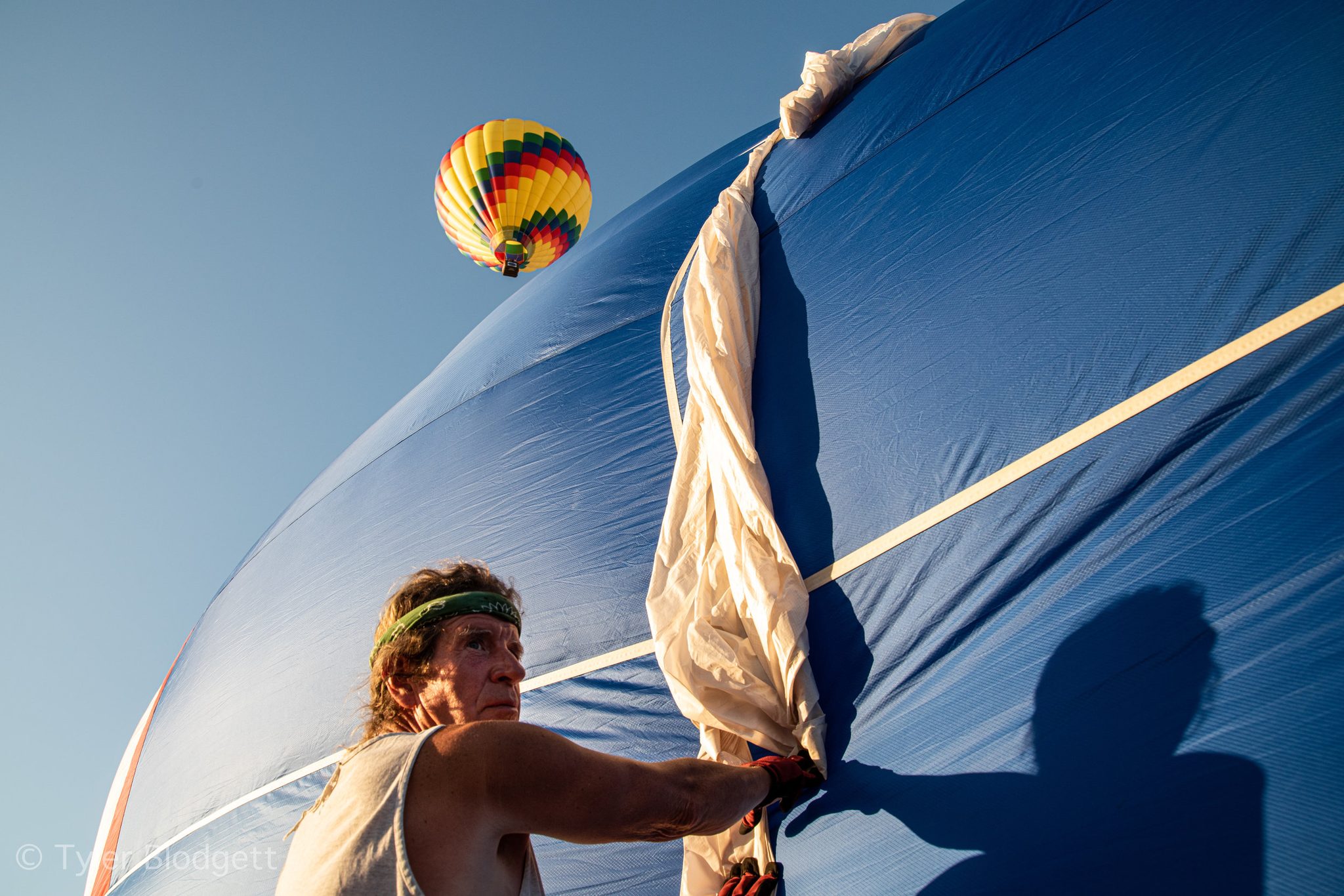A crew member gathers the collapsing fabric, another balloon already rising in the sky.