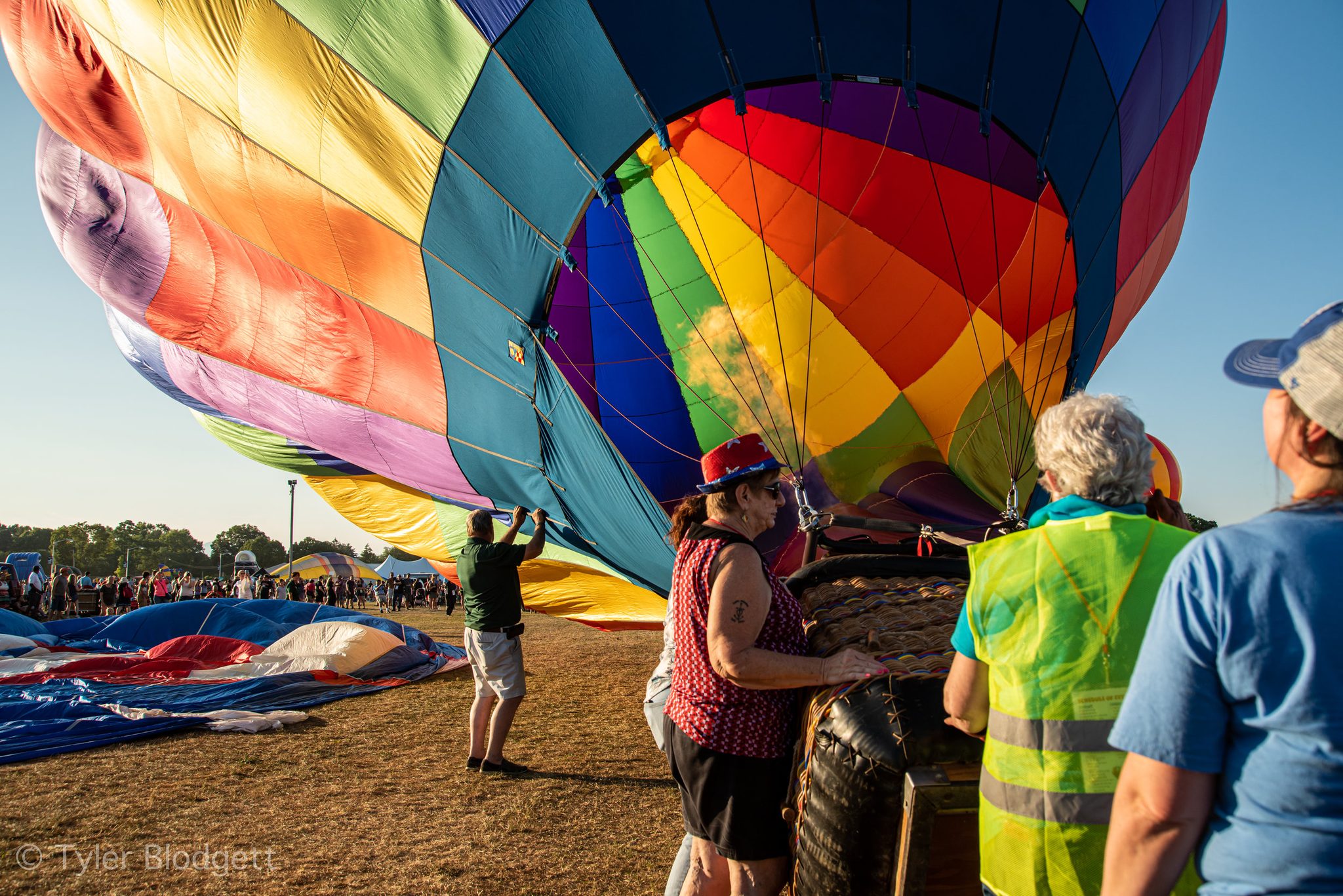 Hands on the ropes, the crew guides a rainbow envelope toward standing.