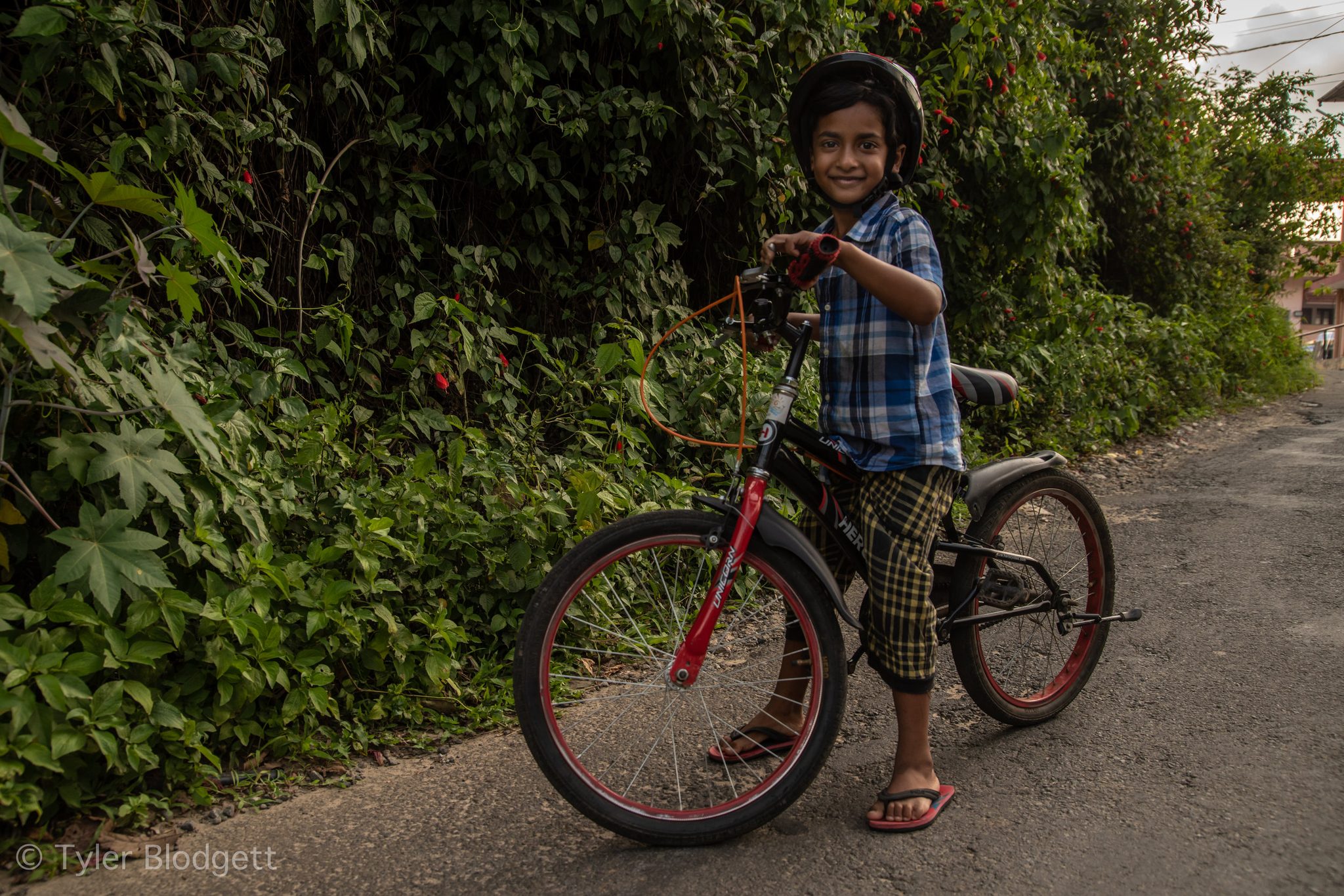 A boy in a helmet grins over his handlebars on a green lane.
