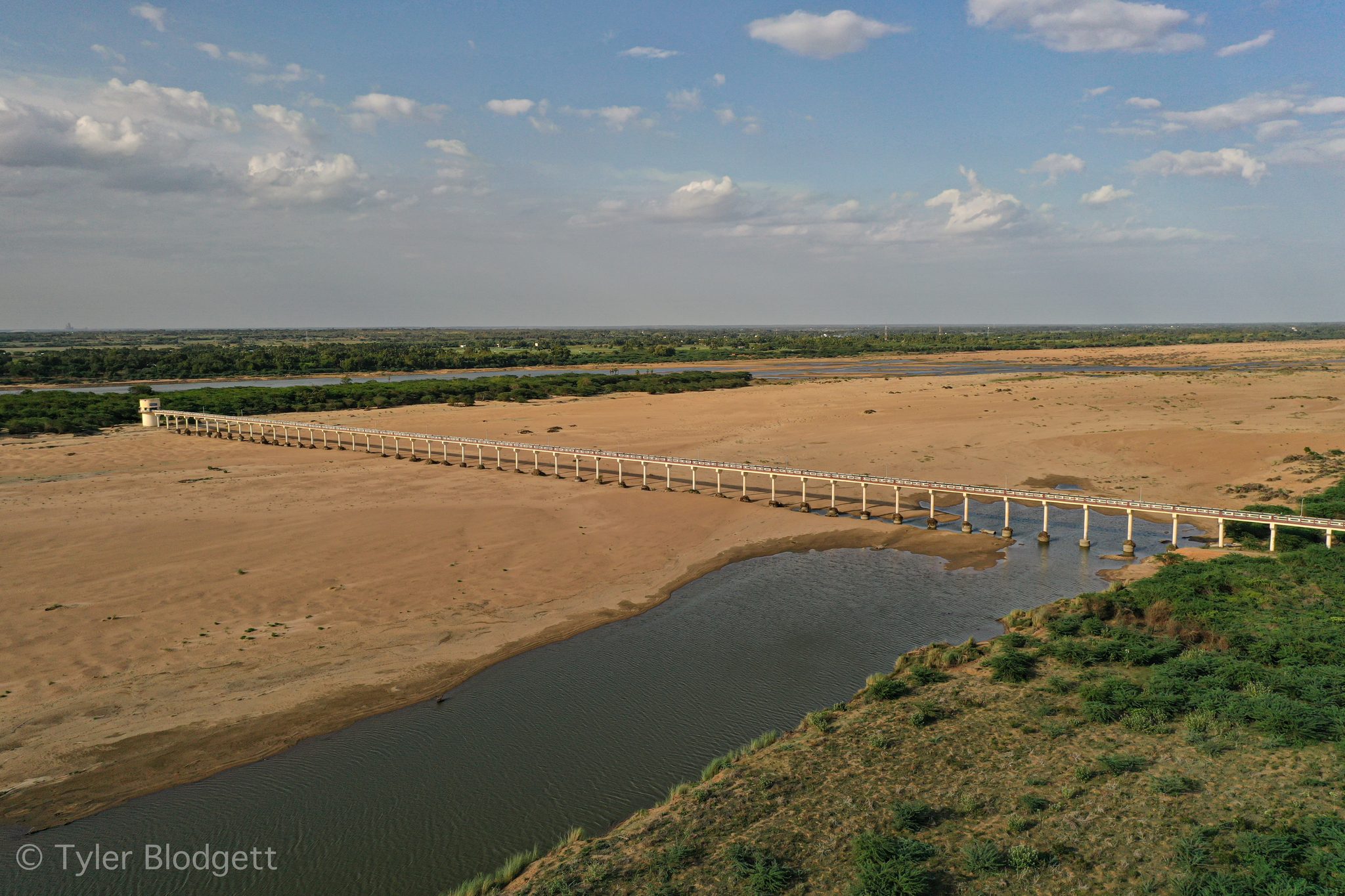A long bridge crosses a riverbed that is mostly sand, the water a narrow channel below.