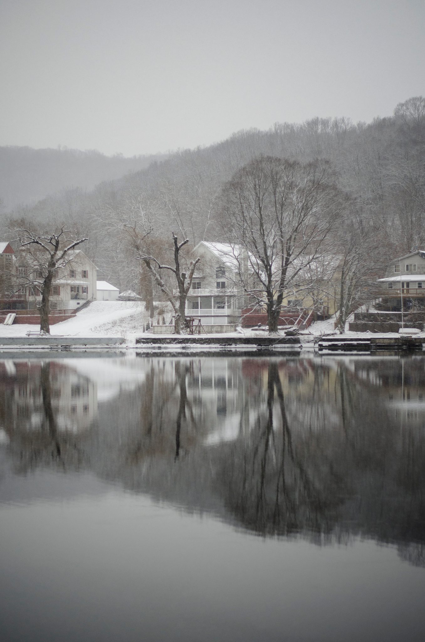 Bare trees and snowy roofs stand on their reflections in the river.
