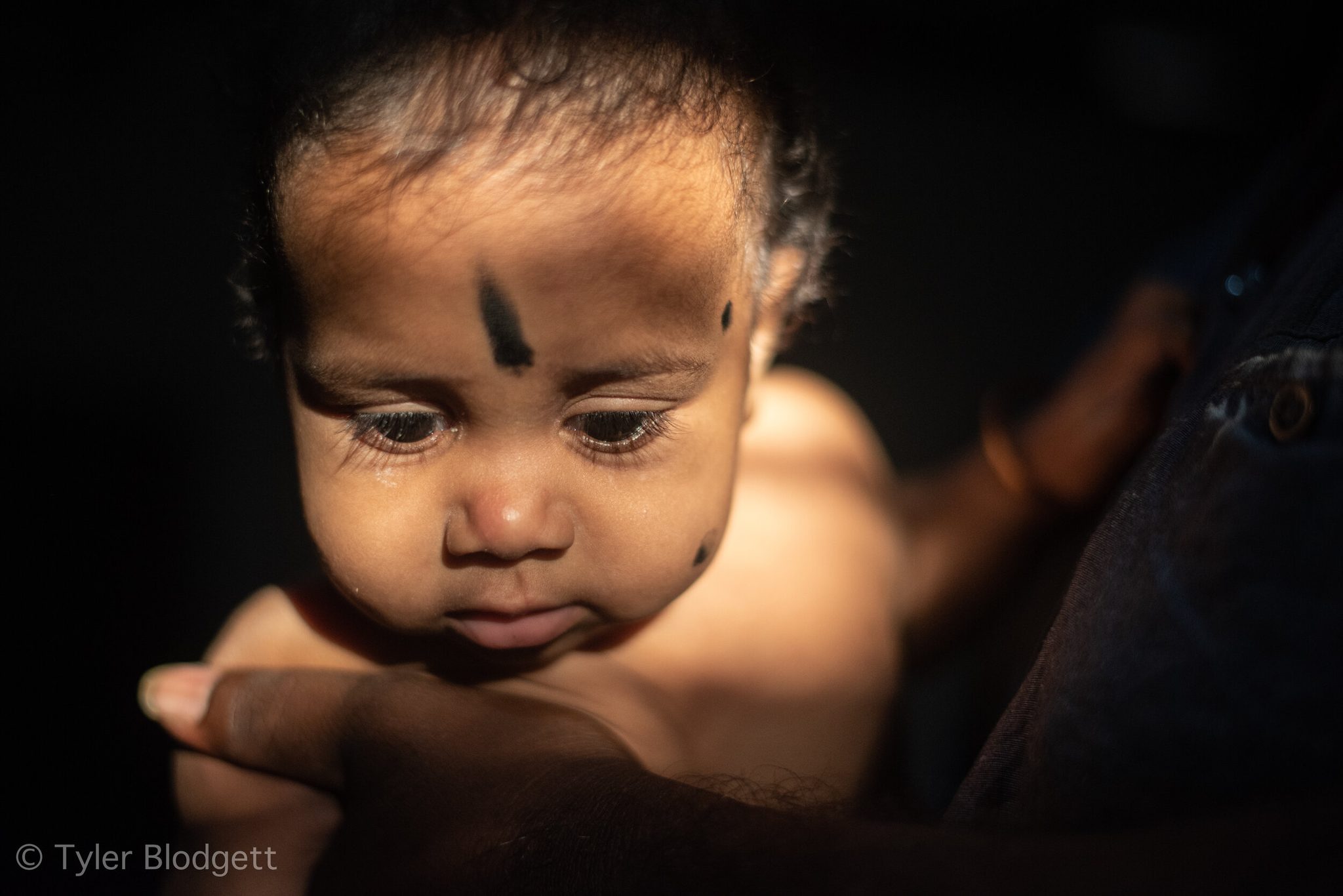 A baby rests in a parent's arms, a smudge of kajal on the forehead to keep the evil eye away.
