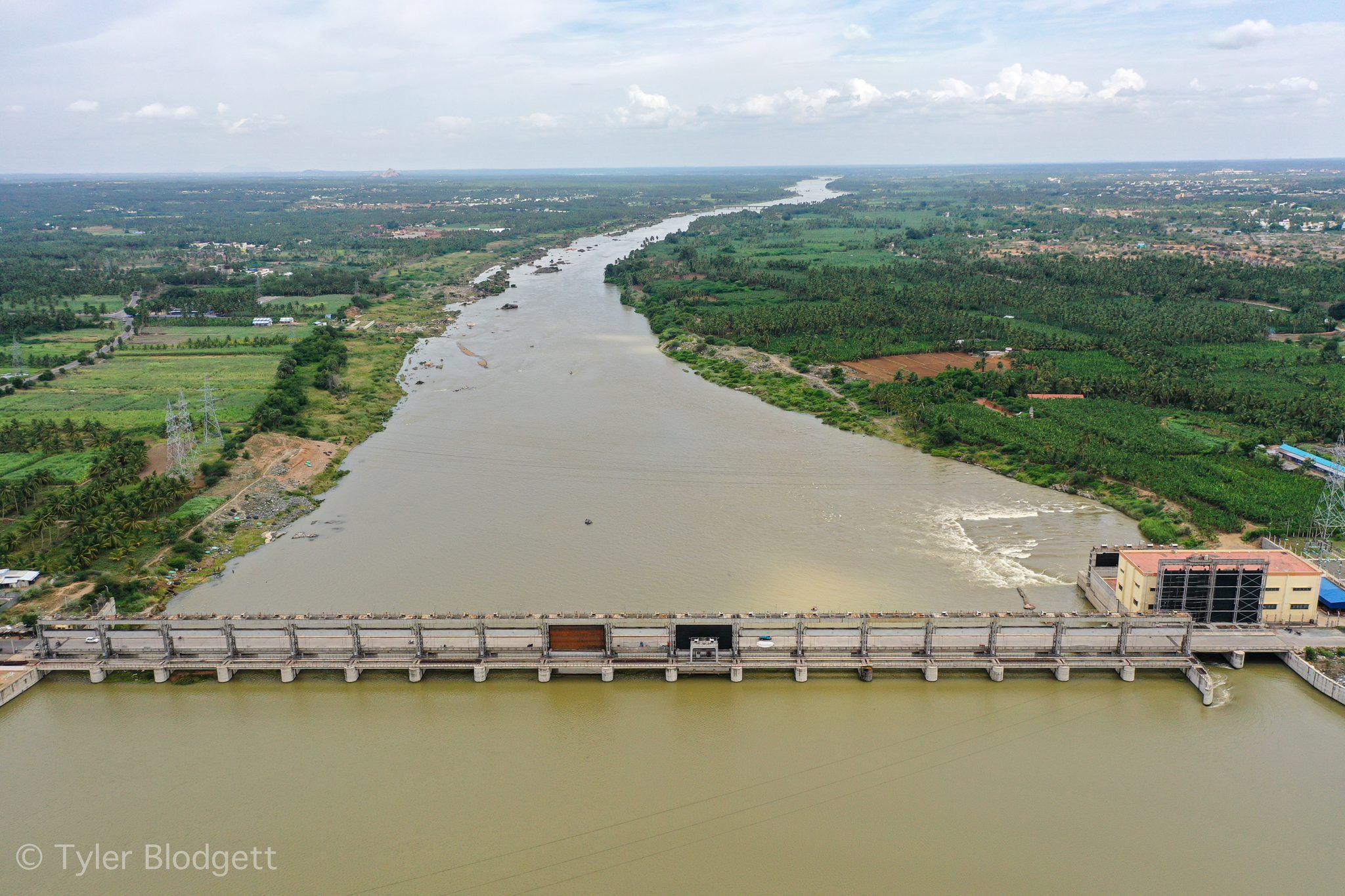 A barrage spans the wide brown river, the farmland stretching away on both banks.