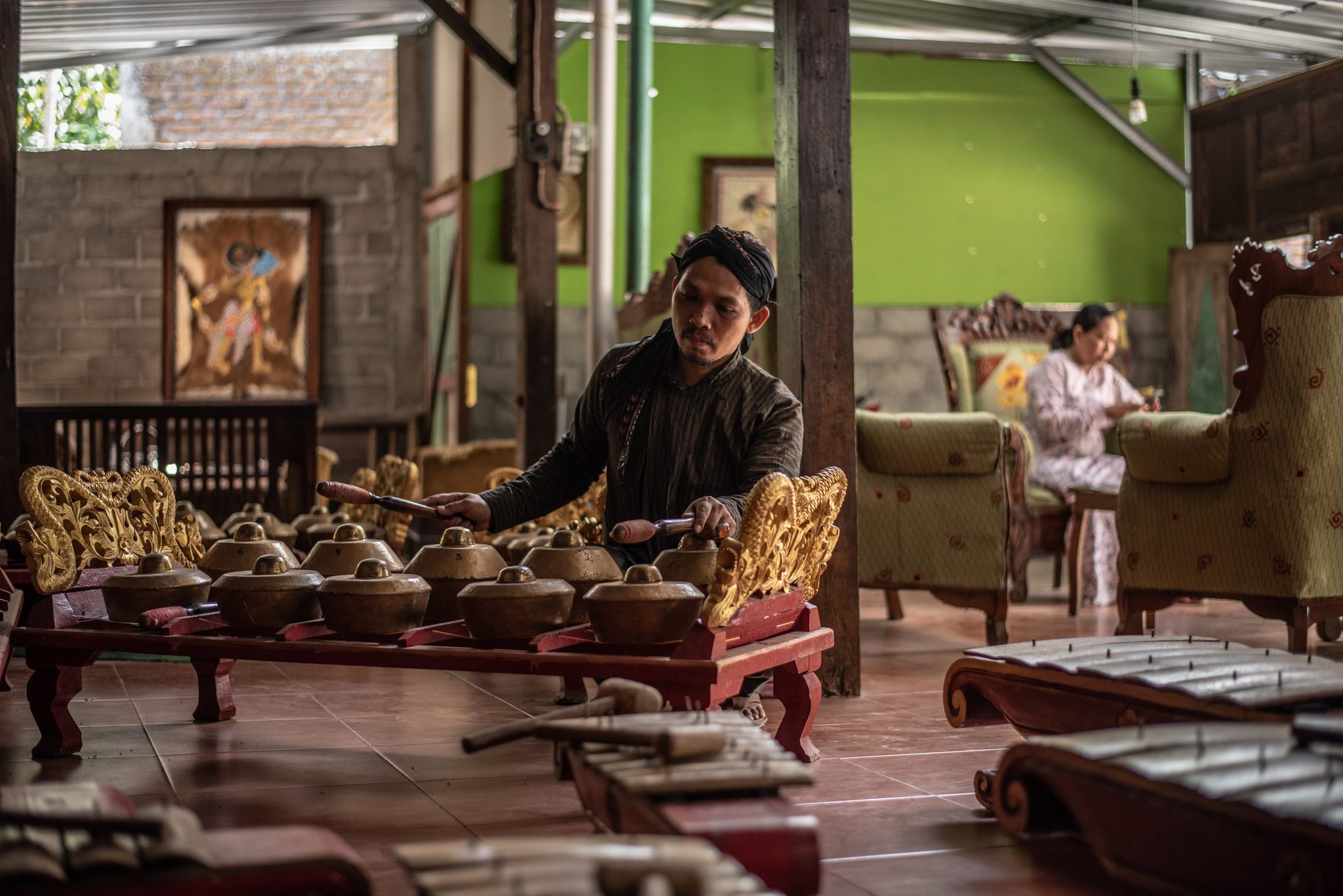 Dhidot plays the gamelan while his wife relaxes in the back ground