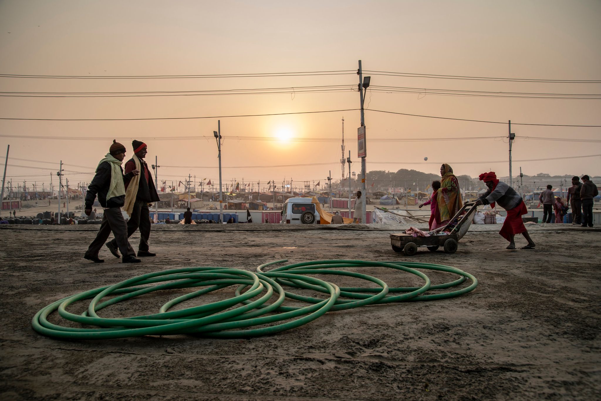 The sun rises weak through the haze as the tent city stirs, a hose coiled on the sand.