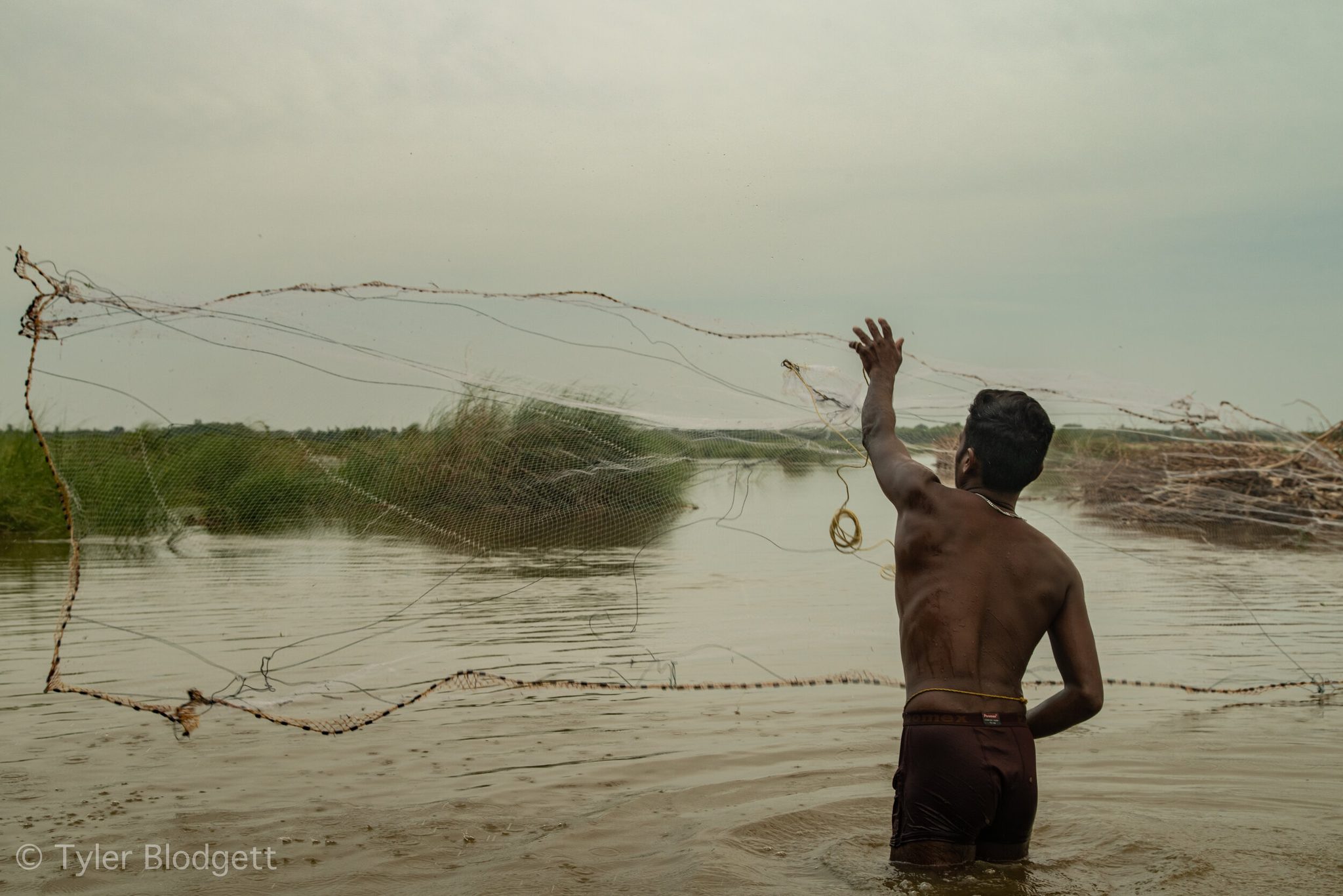A man throws his net wide, and for a moment it hangs in the air like smoke.