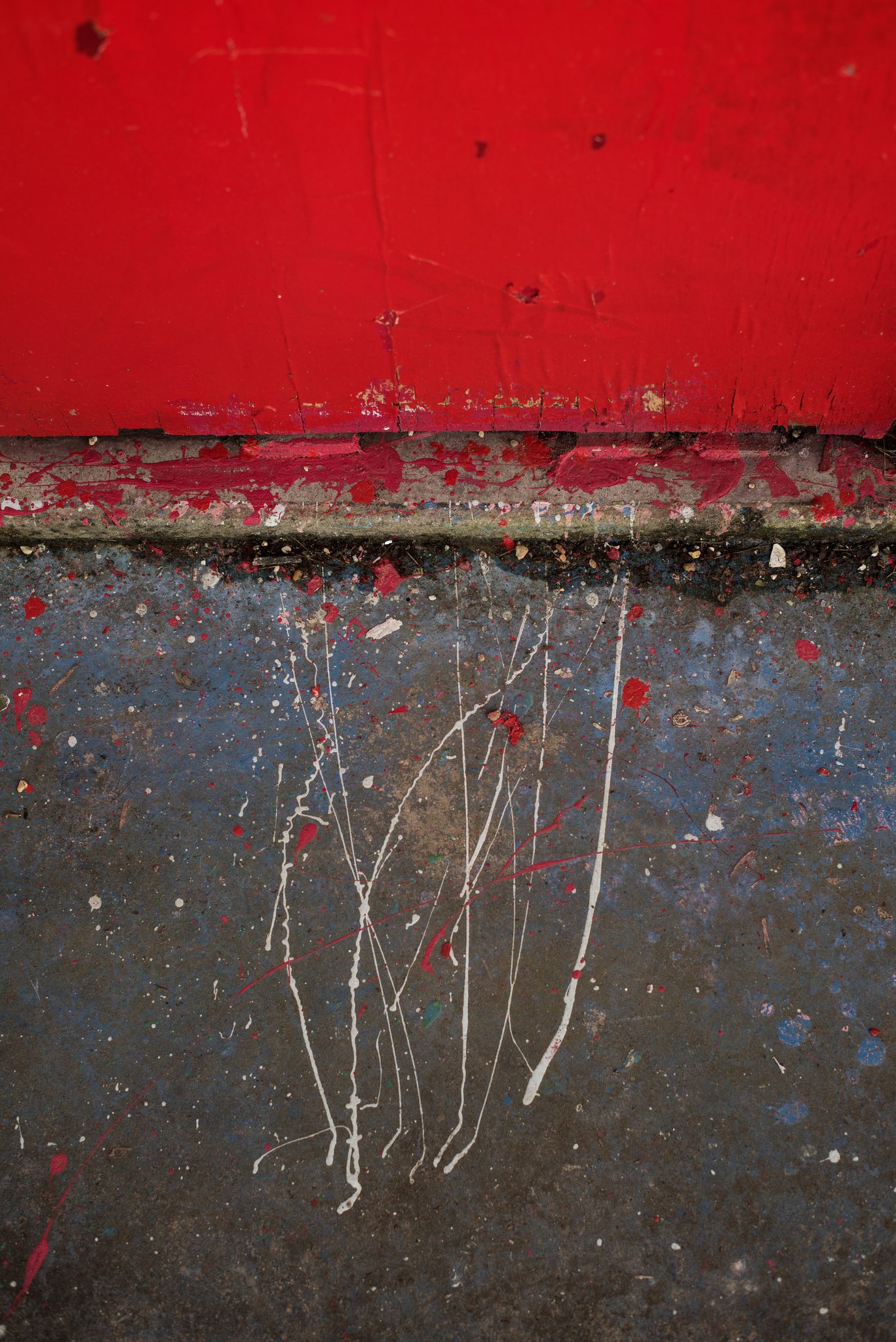 Drips of white paint run down a red and gray wall.