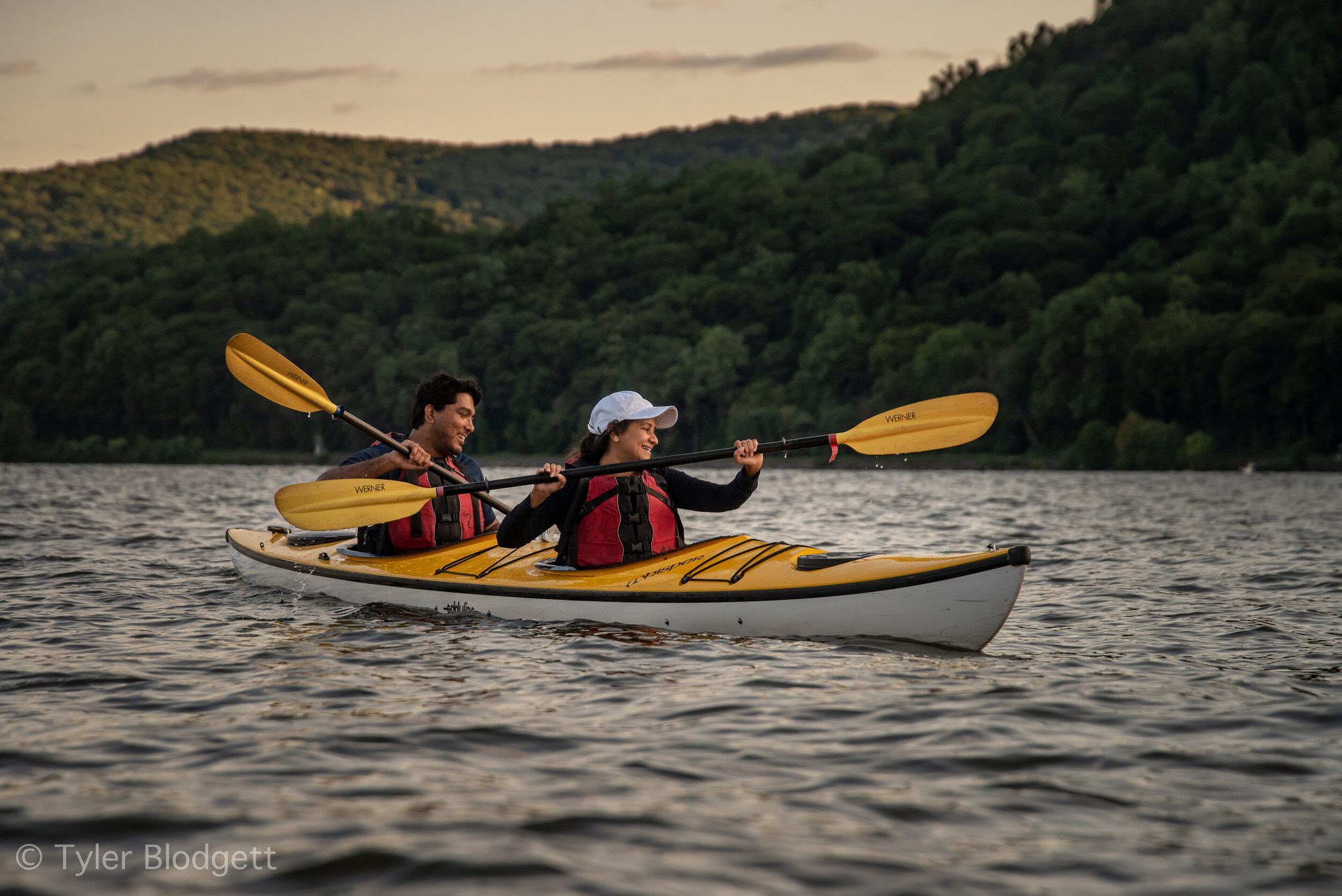 Two paddlers find their rhythm on the river as evening settles over the hills.