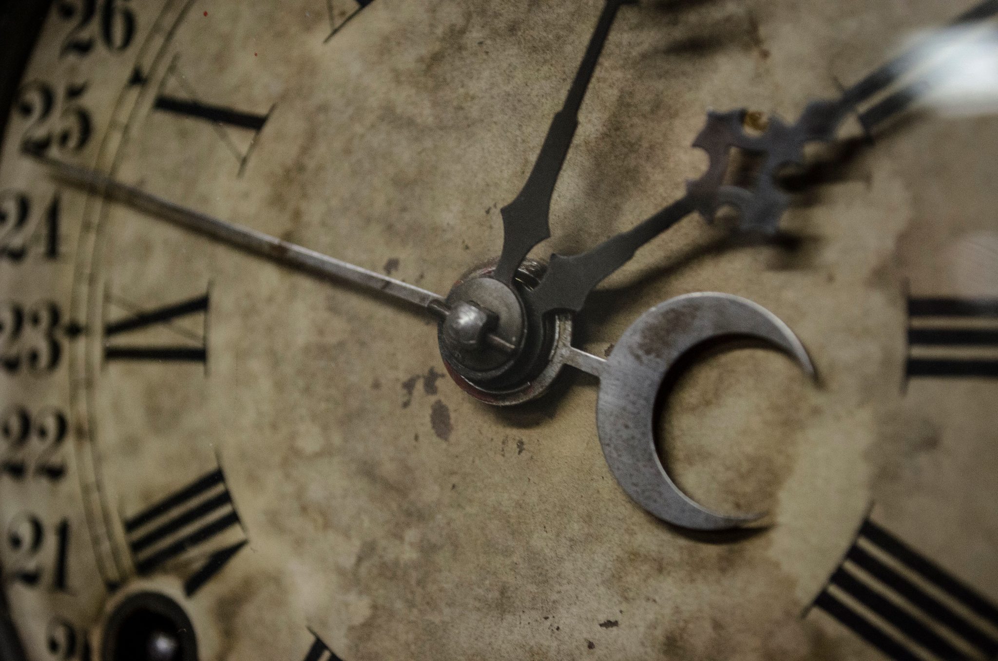 An old clock face with a crescent moon on its hand, the paint worn and stained.