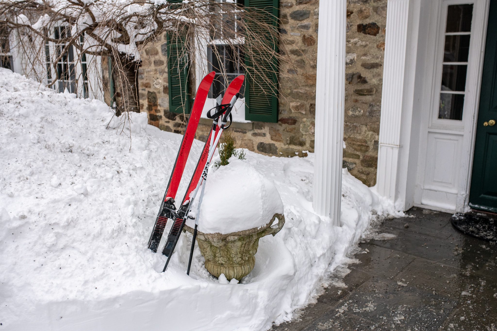 Skis propped by the front door beside an urn buried in snow.