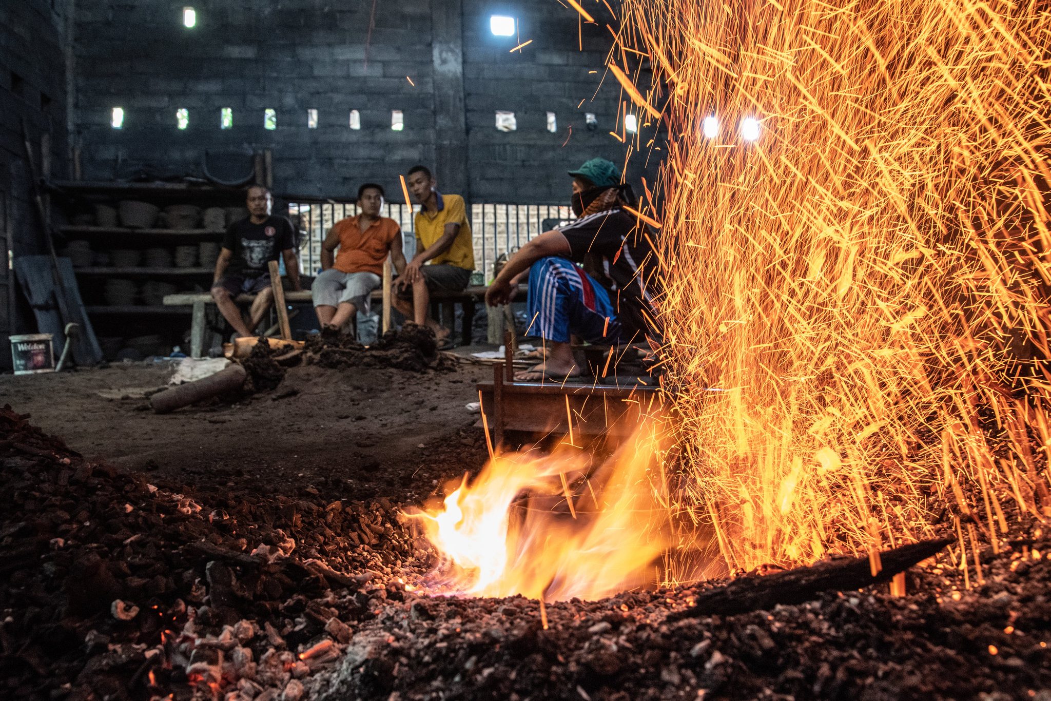 The forge erupts in a column of sparks while the blacksmiths watch from the bench. There was something profound in these moments, when flame begot music.