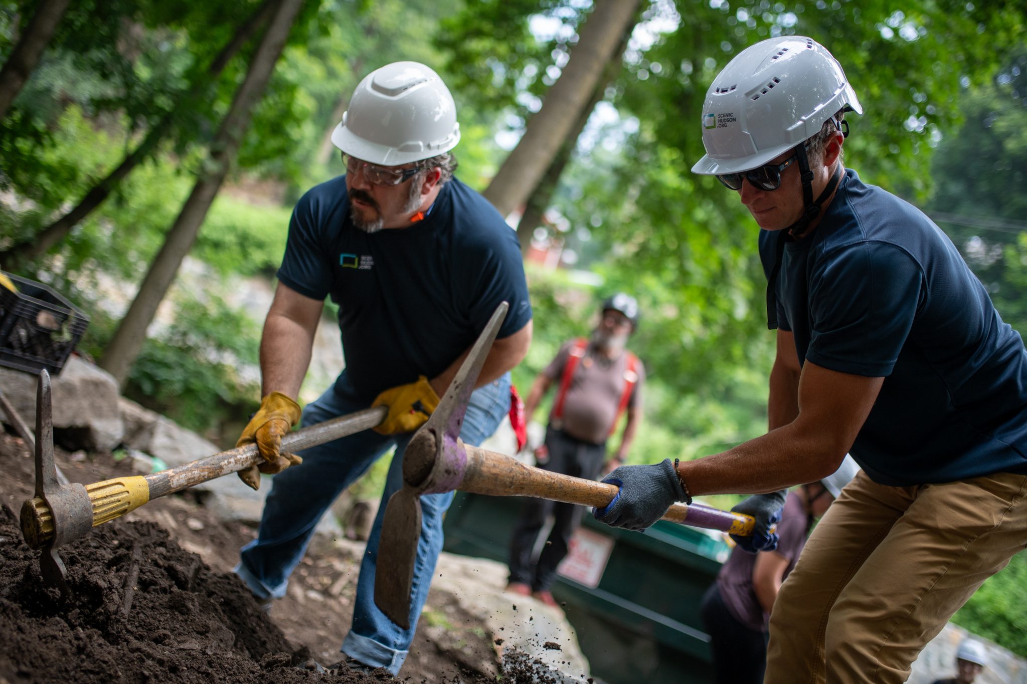 Two crew members swing their mattocks in rhythm.