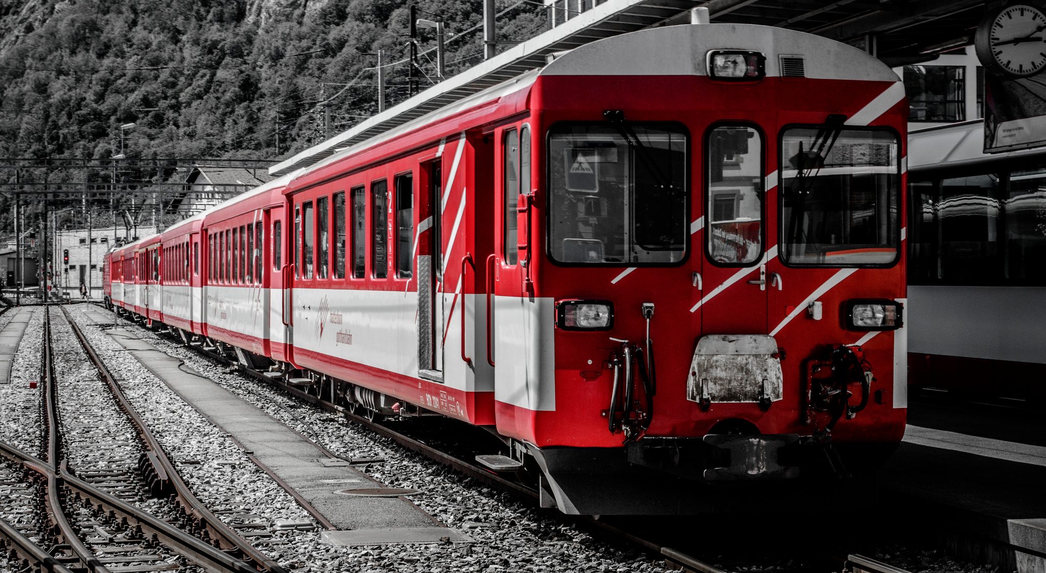 A red train waits on the tracks, the only color at the station.