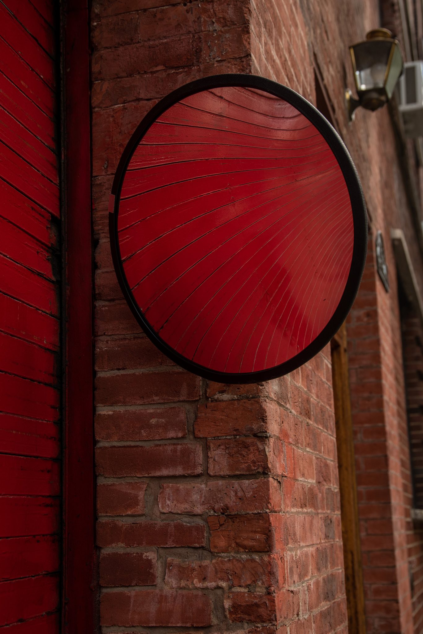 A red disc hangs against a red wall, a single lamp above it.