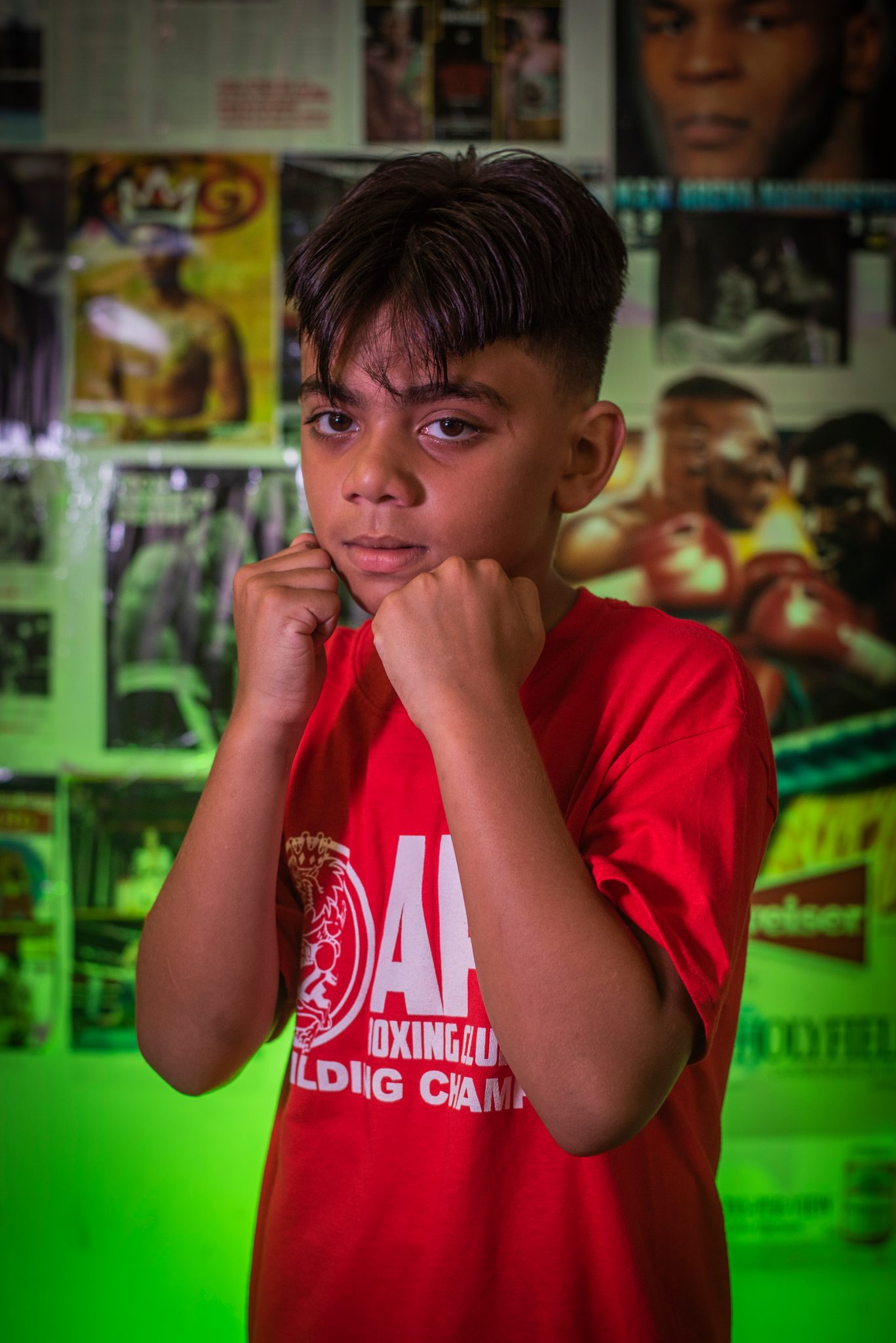 A young boxer squares up under the green light, fists at his chin.
