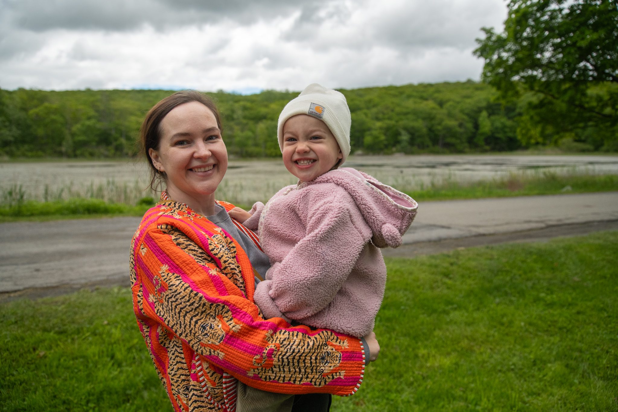A mother holds her smiling toddler by the pond.