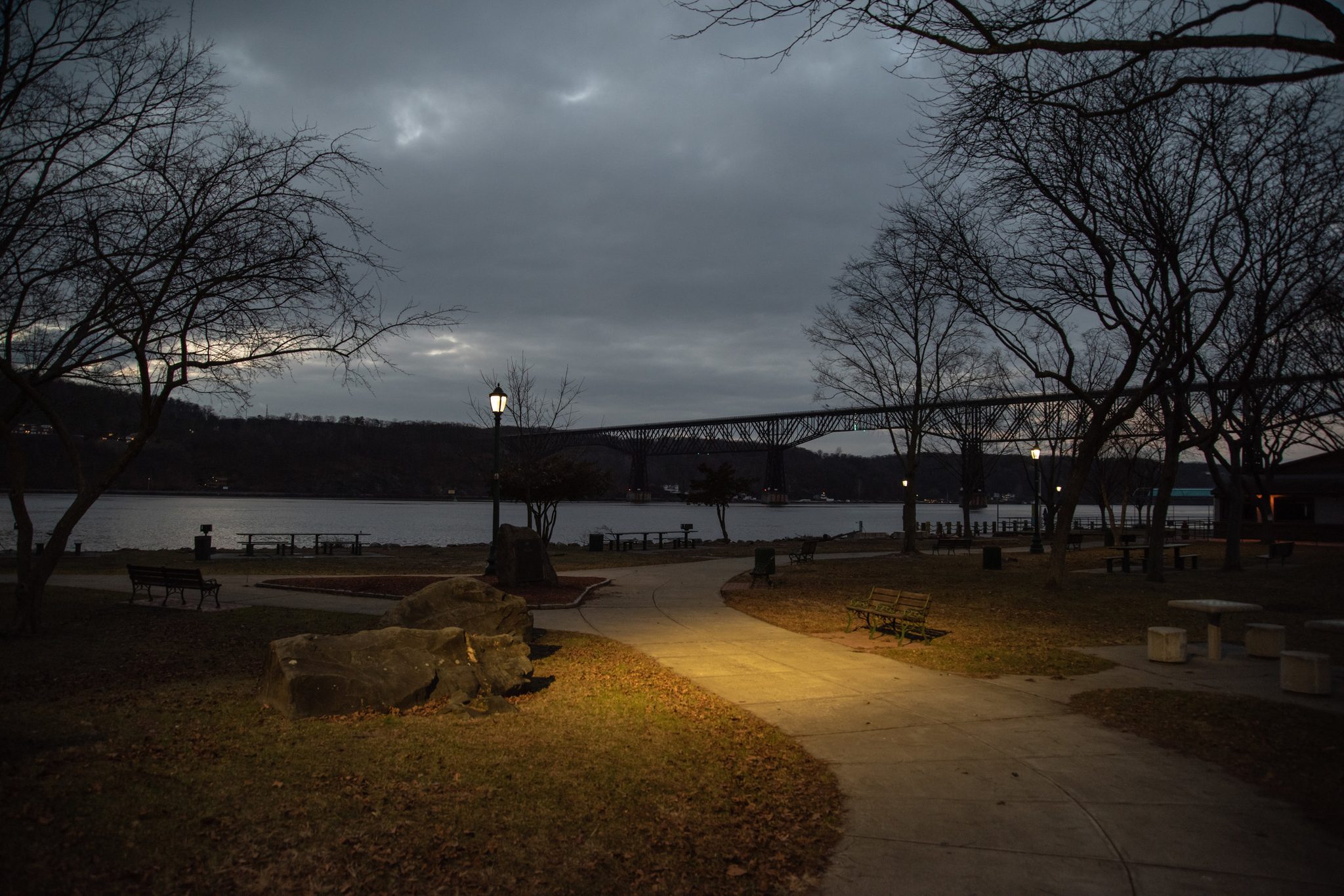 Lamps come on along the riverside path, the Walkway Over the Hudson stretched across the dusk.