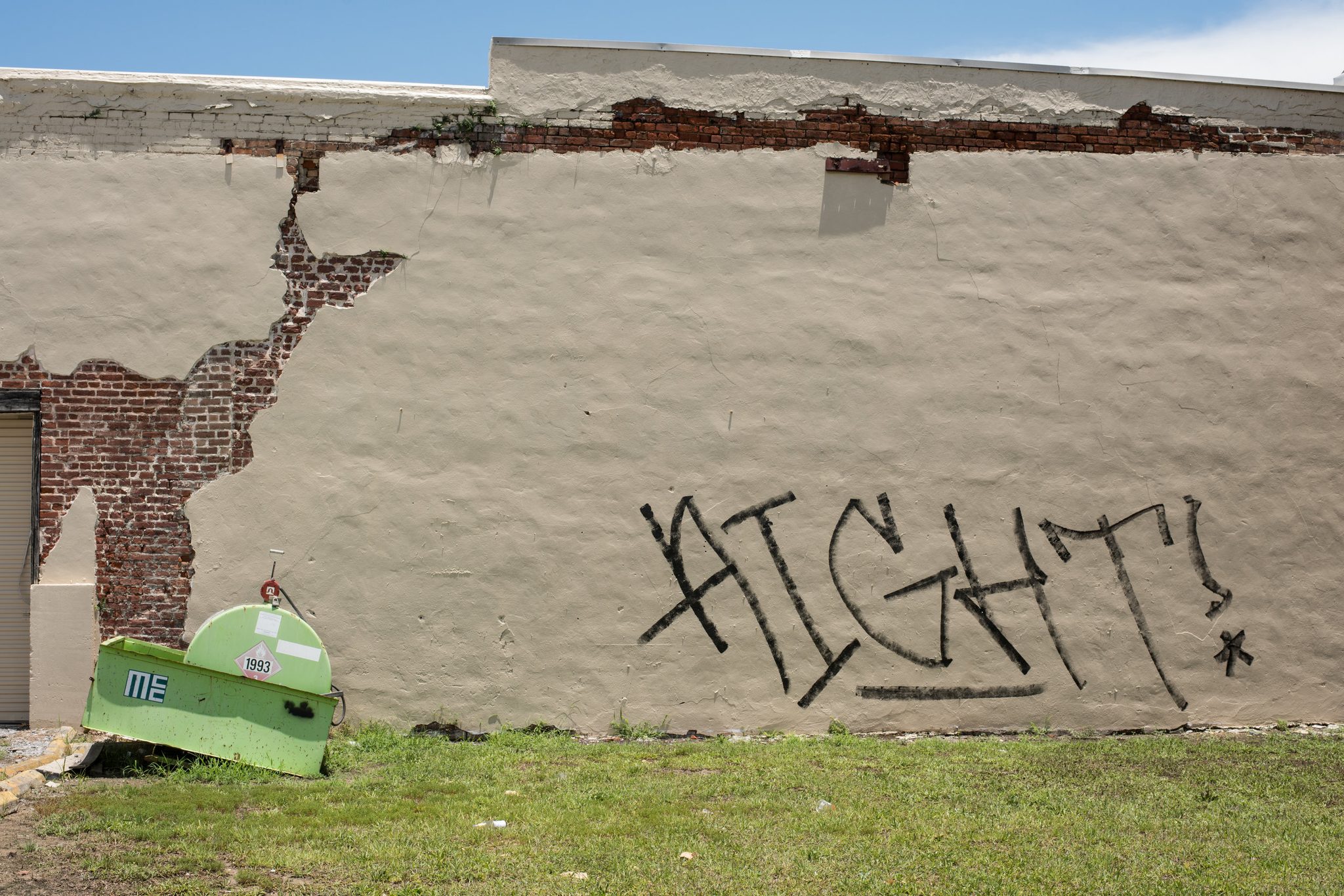 AIGHT!, scrawled across a cracked wall, as if in answer to the broken dumpster below.