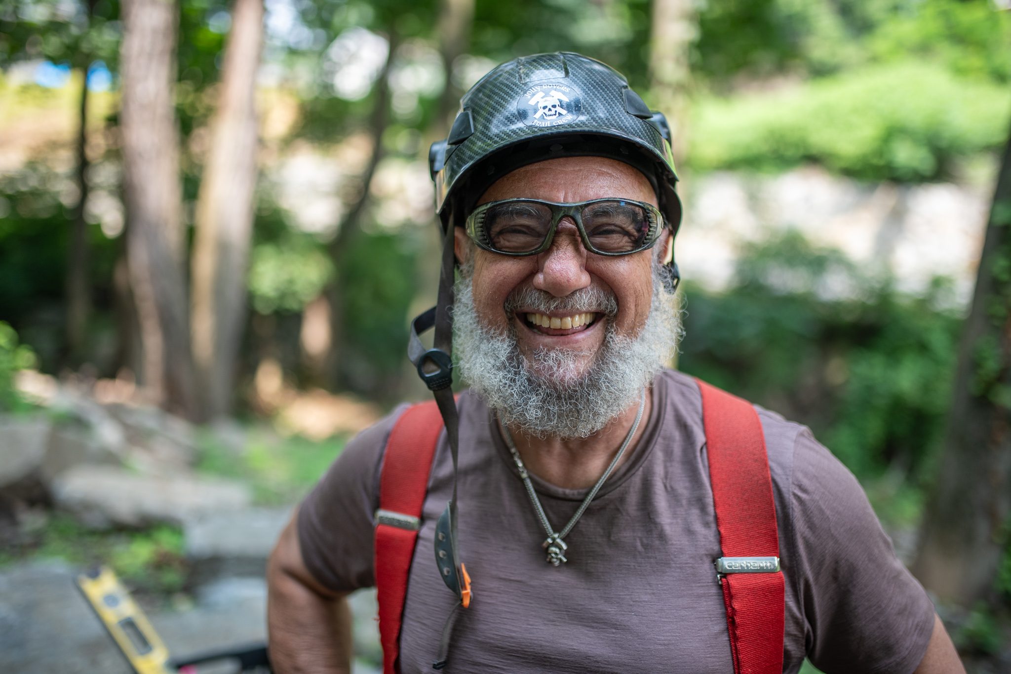 The crew leader grins behind his goggles, beard and suspenders dusty from the day.