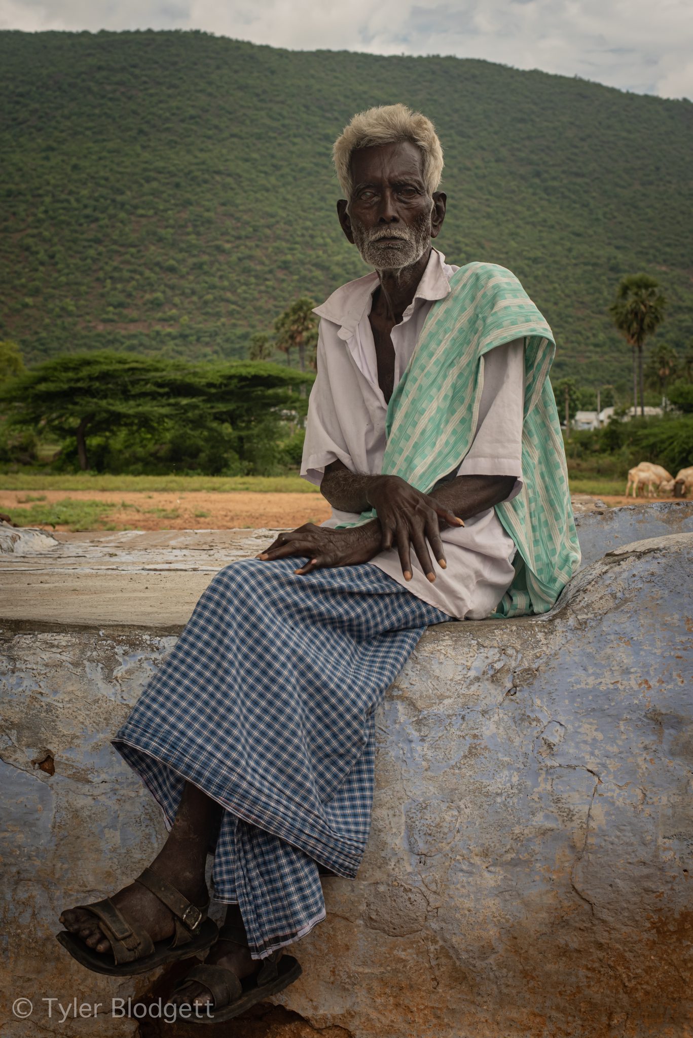 He sits on a blue-painted wall, hands resting on his knees.