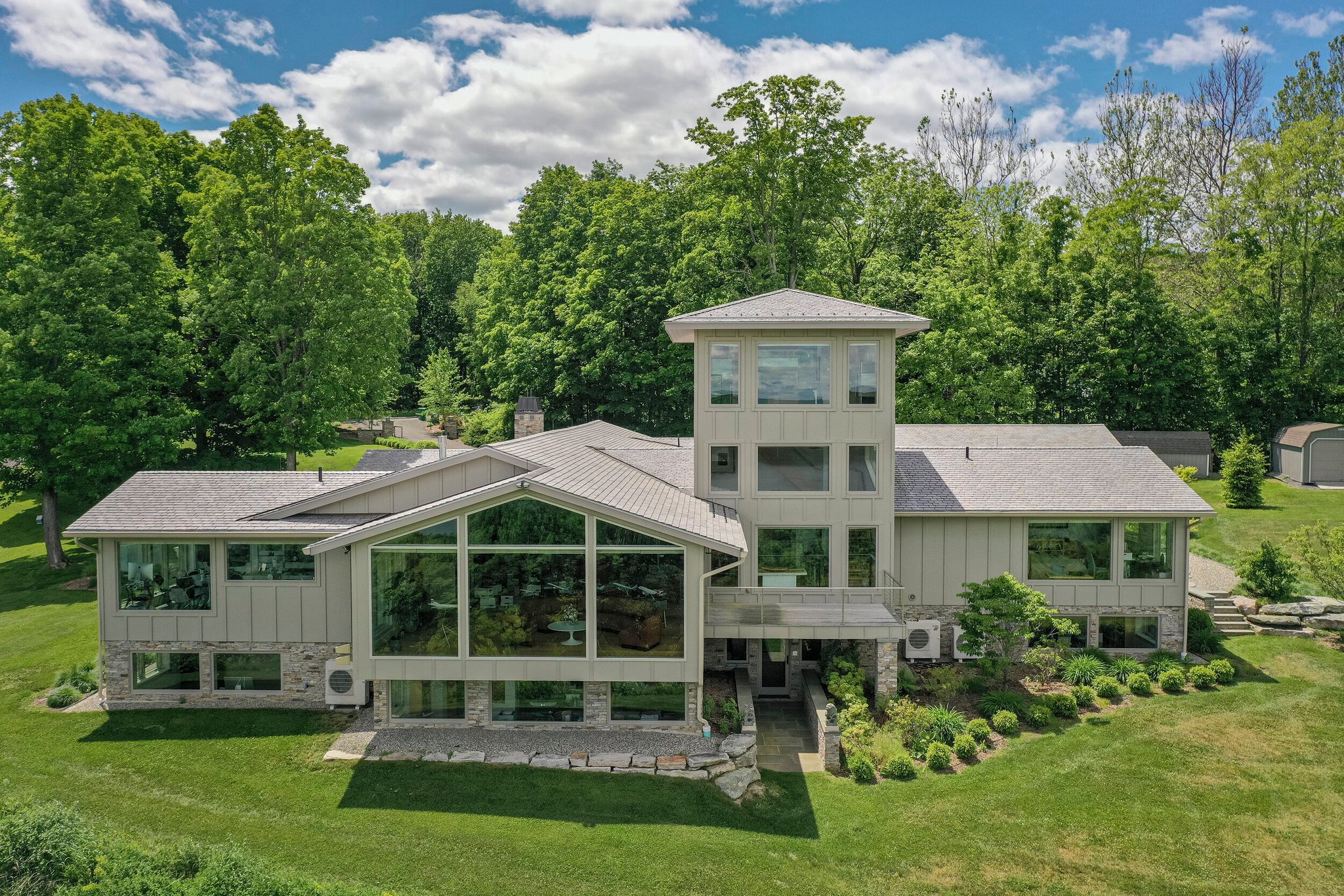 A glass tower rises from the middle of the house, the lawn rolling out to the trees.