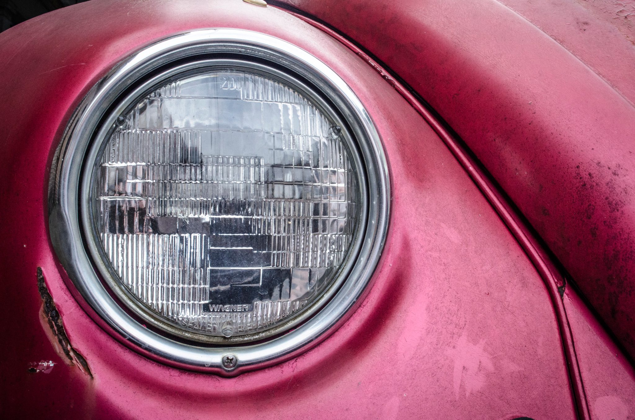 The headlight of an old pink Beetle, dented and dusty.