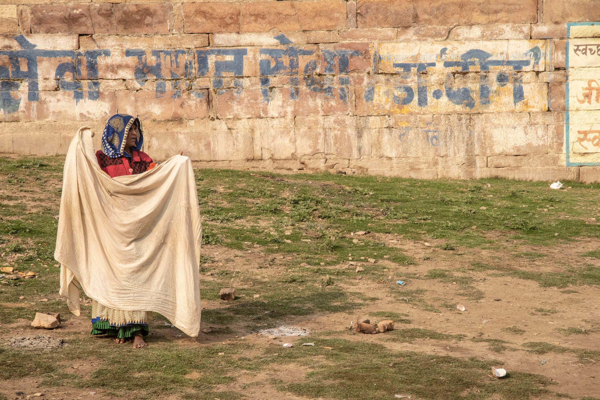 Woman stands afield, drying clothes in the sun