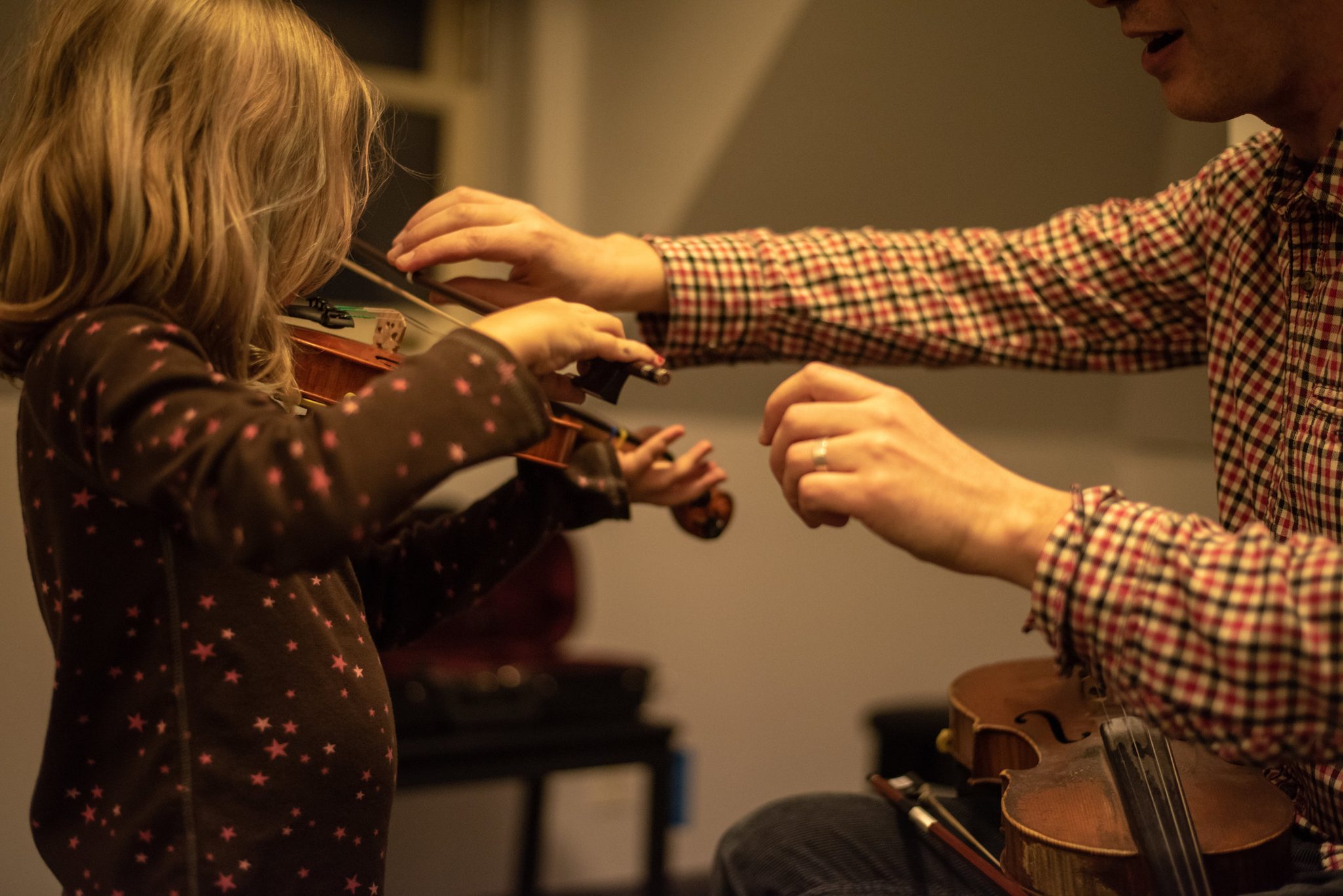 A young student raises her violin while Tom guides her bow arm.