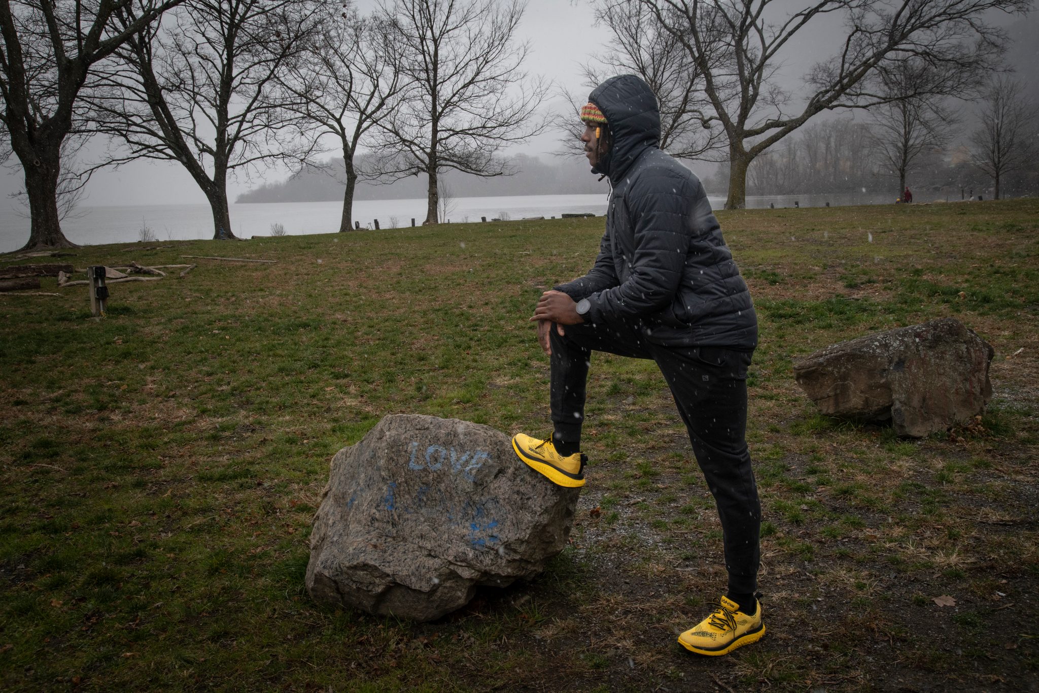 One foot up on a painted boulder, Chev pauses under bare trees with the river fogged in behind.
