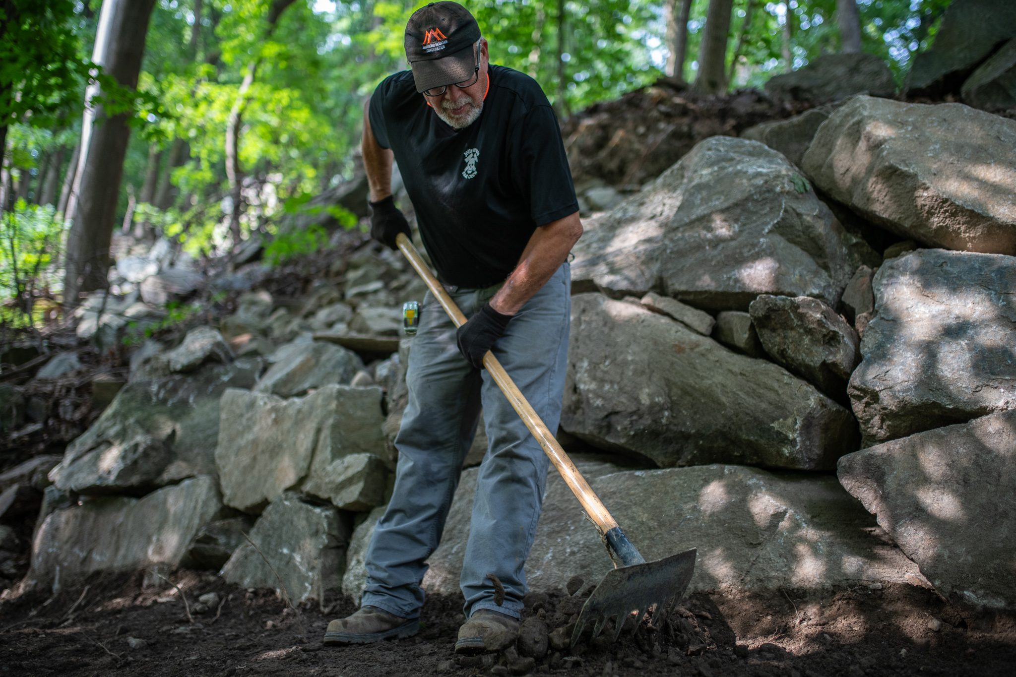 A crew member digs in with a shovel below a wall of boulders.