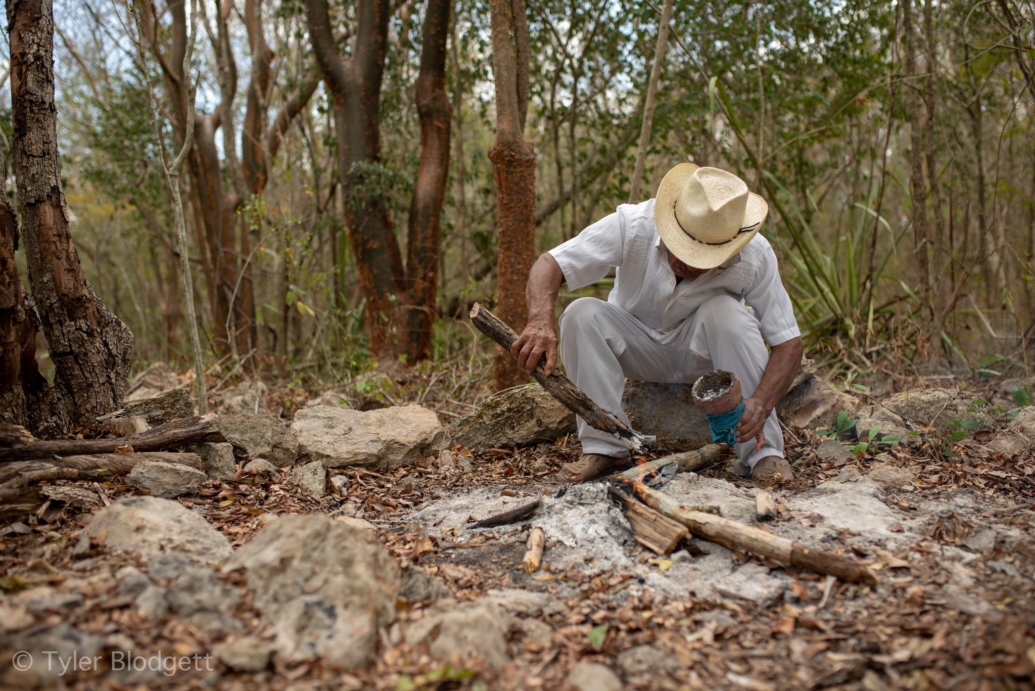 He crouches to tend the fire before the ceremony begins.