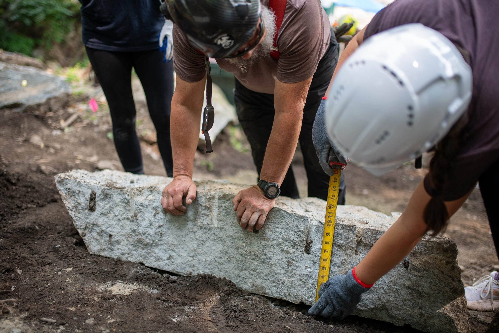 Two crew members measure a step that is half set in the dirt.
