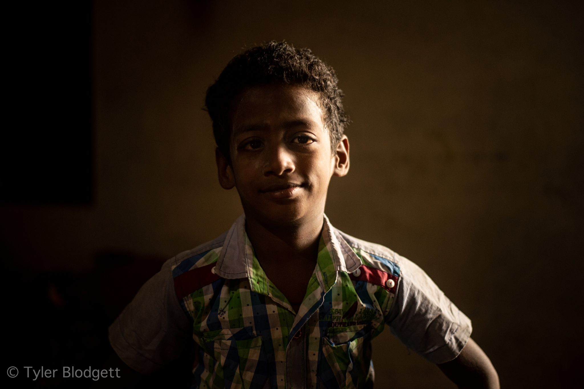 A boy smiles out of the shadows, a sliver of light across his face.