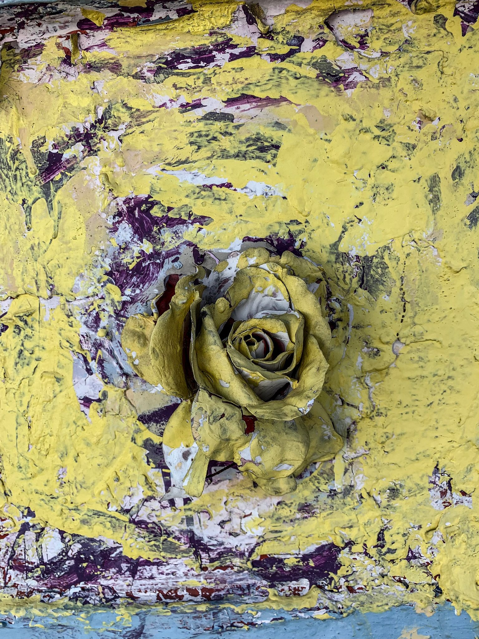 A painted rose blooms out of layers of peeling yellow paint.