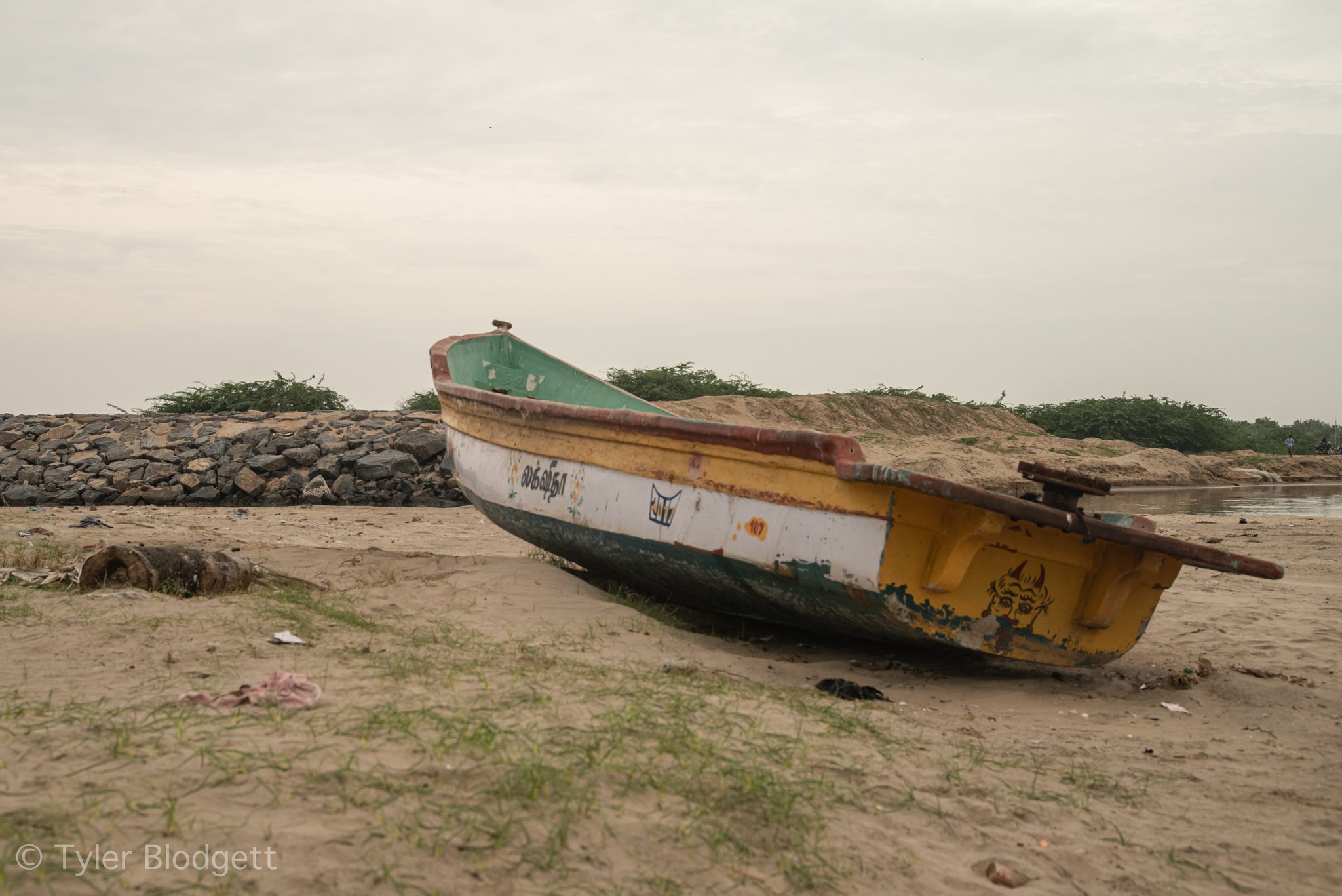 A yellow and white boat leans on the sand beside the rocks.