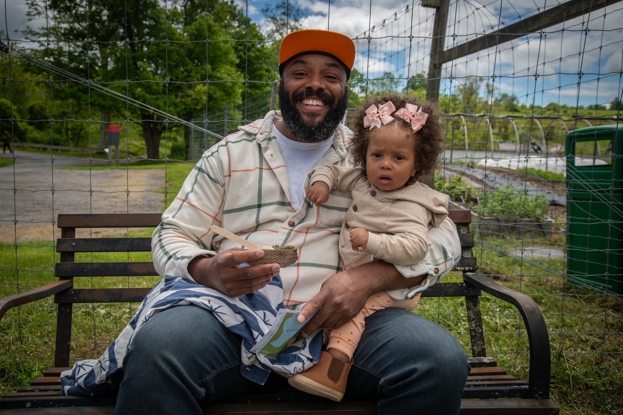 A father laughs on a bench with his daughter in his lap.
