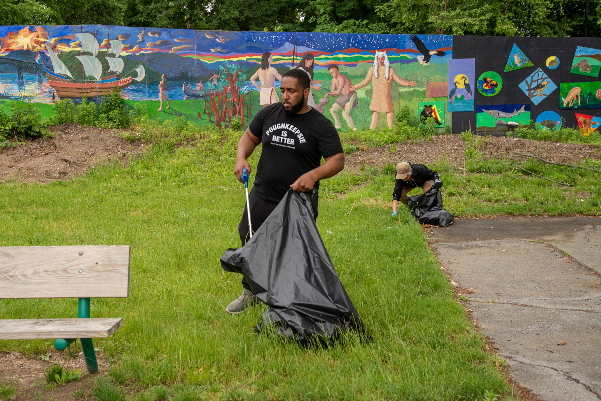 A volunteer drags a full bag across the grass in front of a painted wall.