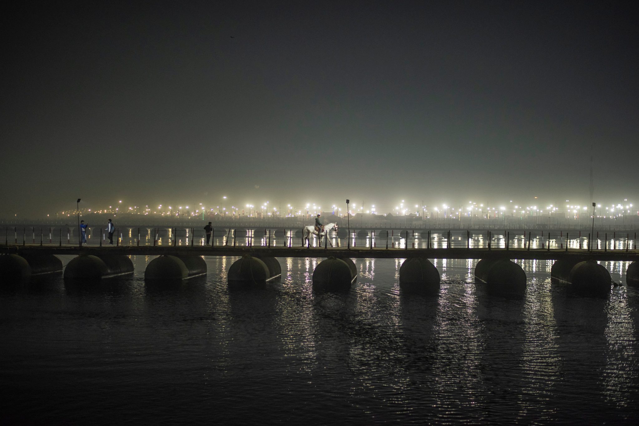 A lone white horse and its rider cross the temporary bridge towards Sangam