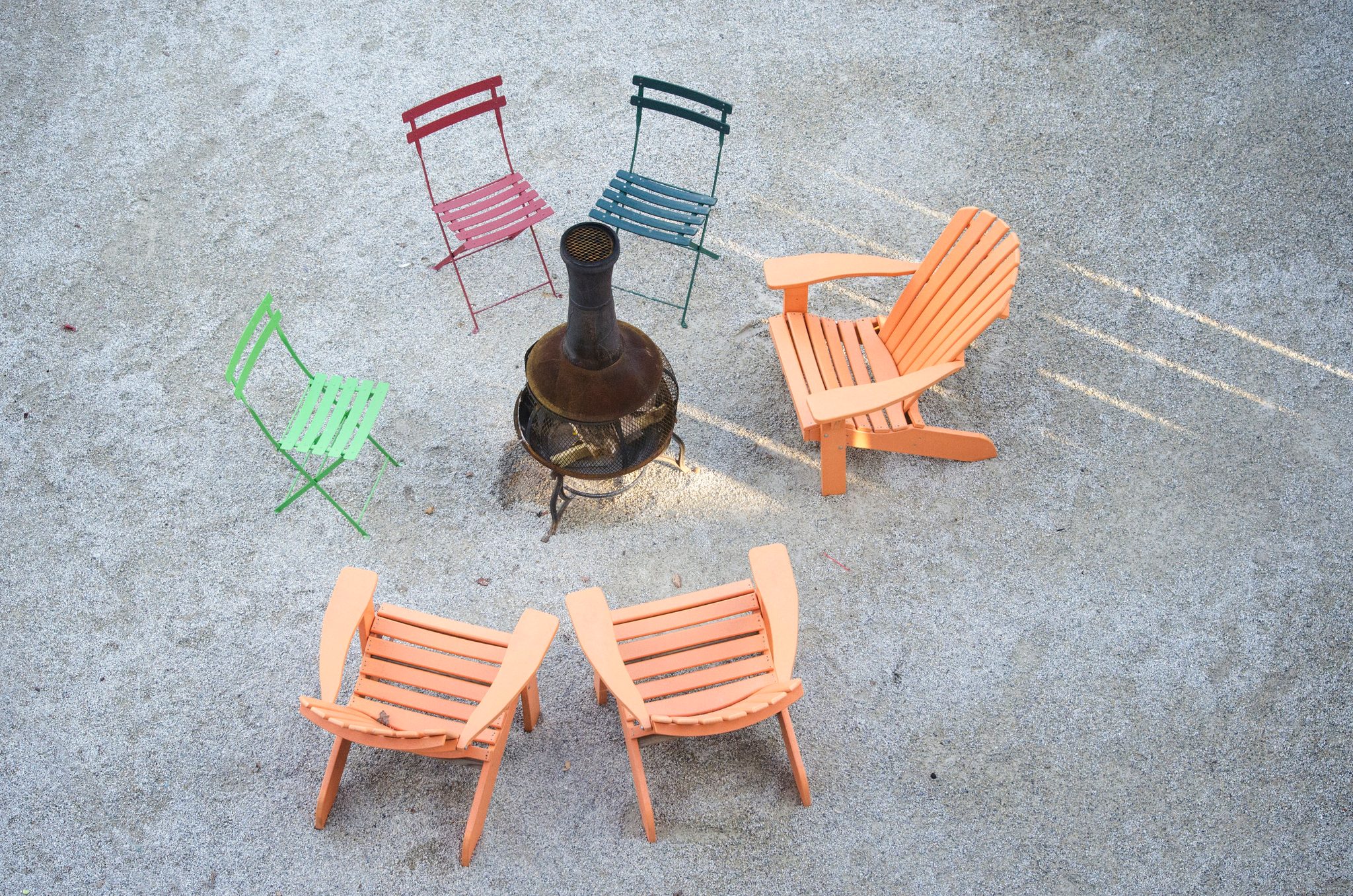 Mismatched chairs circle a chiminea in the sand.