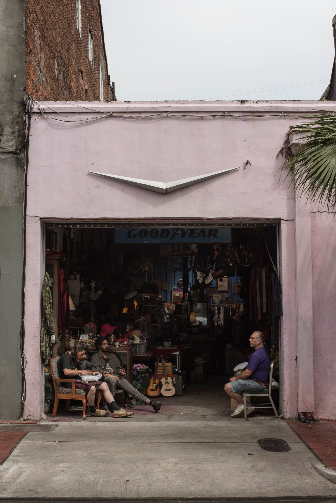 Friends sit in the open garage of a pink thrift shop, guitars on the wall behind them.